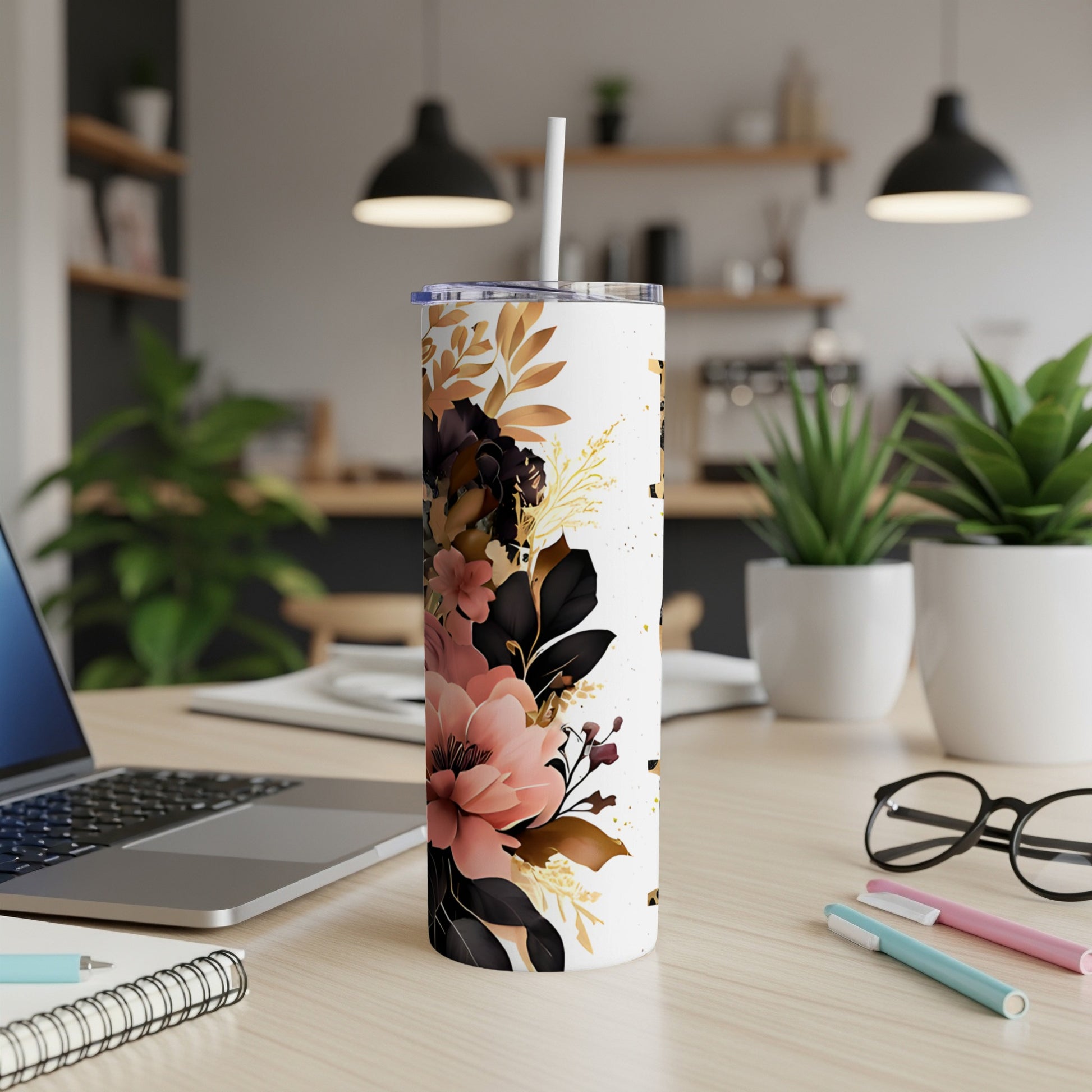 White tumbler with floral and gold splatter design, straw inserted, on a desk.