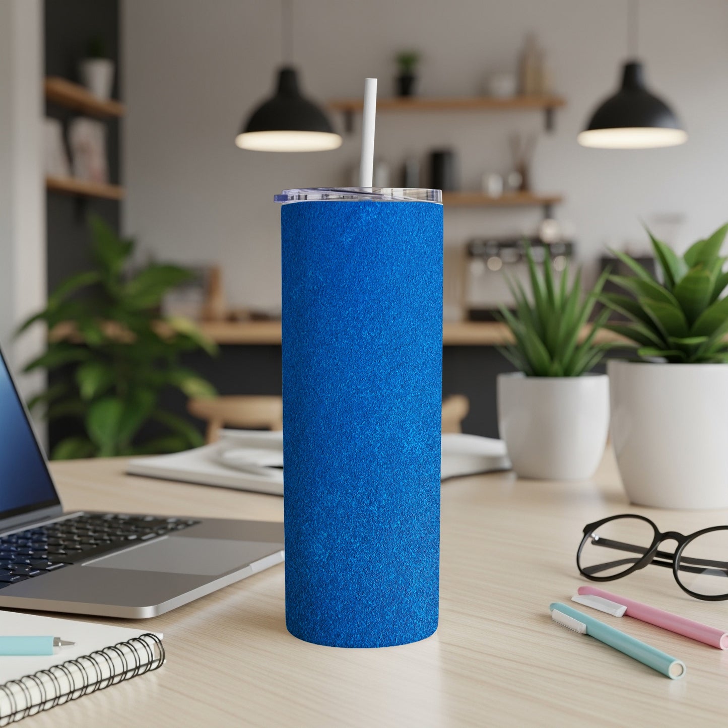 Blue glitter tumbler with straw on a wooden desk.