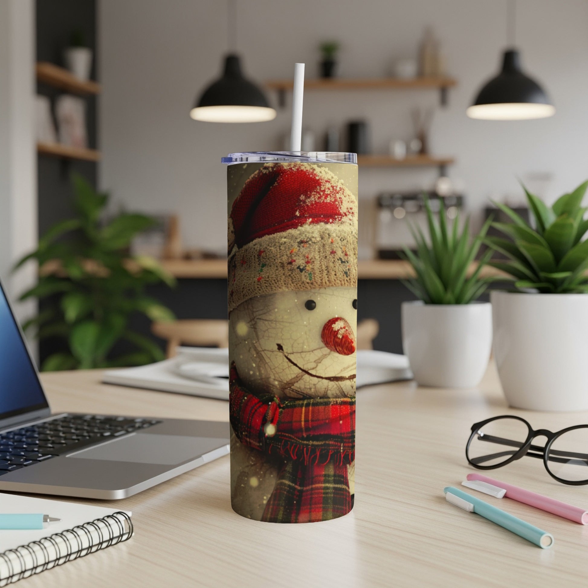 Snowman tumbler with red plaid scarf, Santa hat, and straw on desk.