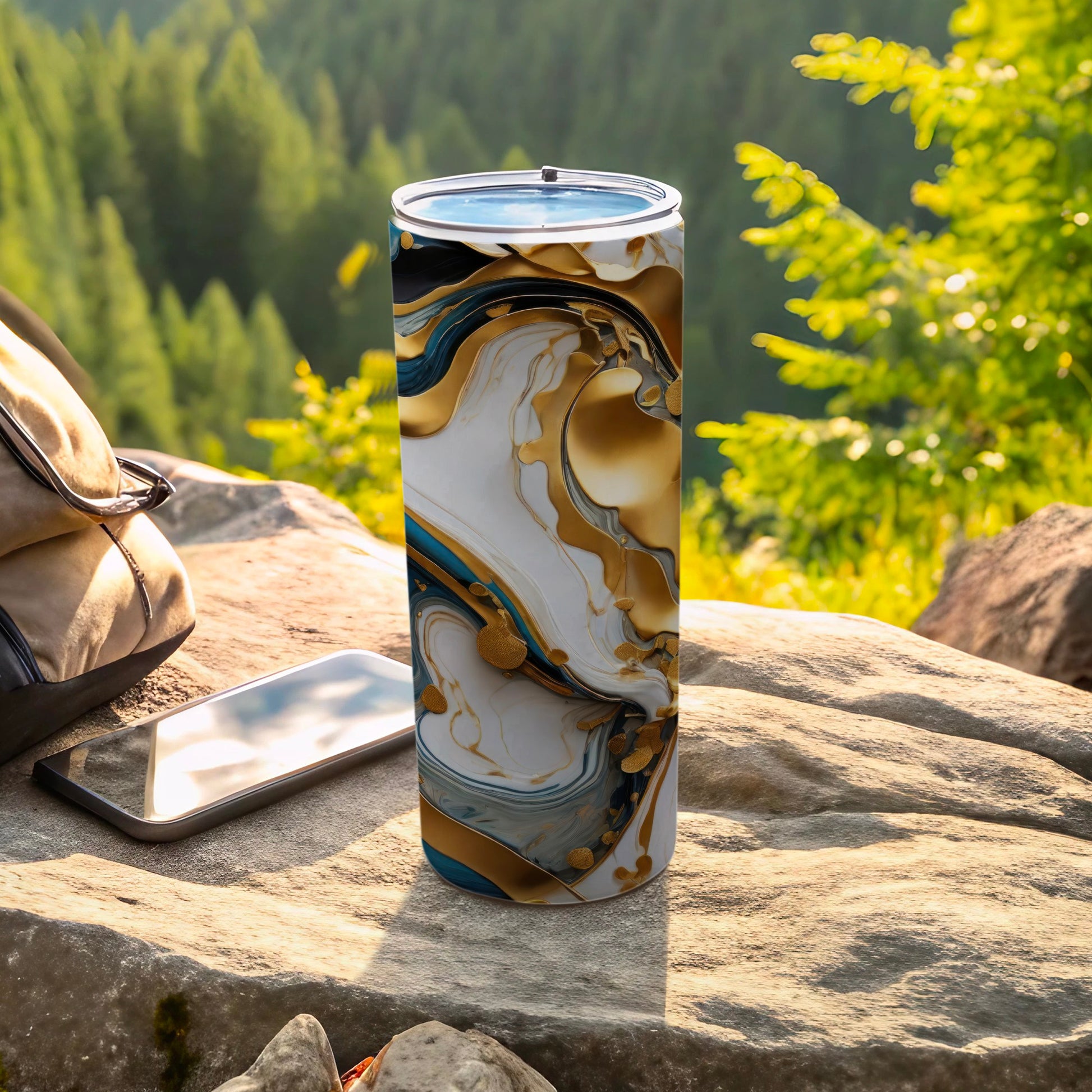 Tumbler with marbled gold and white abstract design next to phone and backpack.