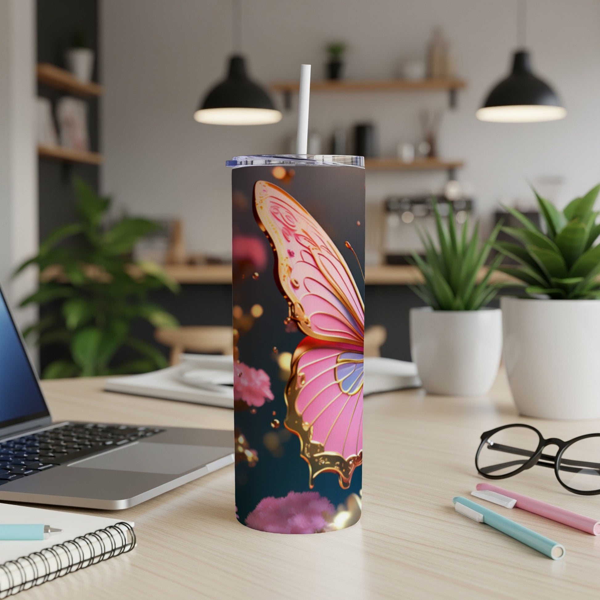 Pink butterfly tumbler with straw on a desk with laptop and pens.