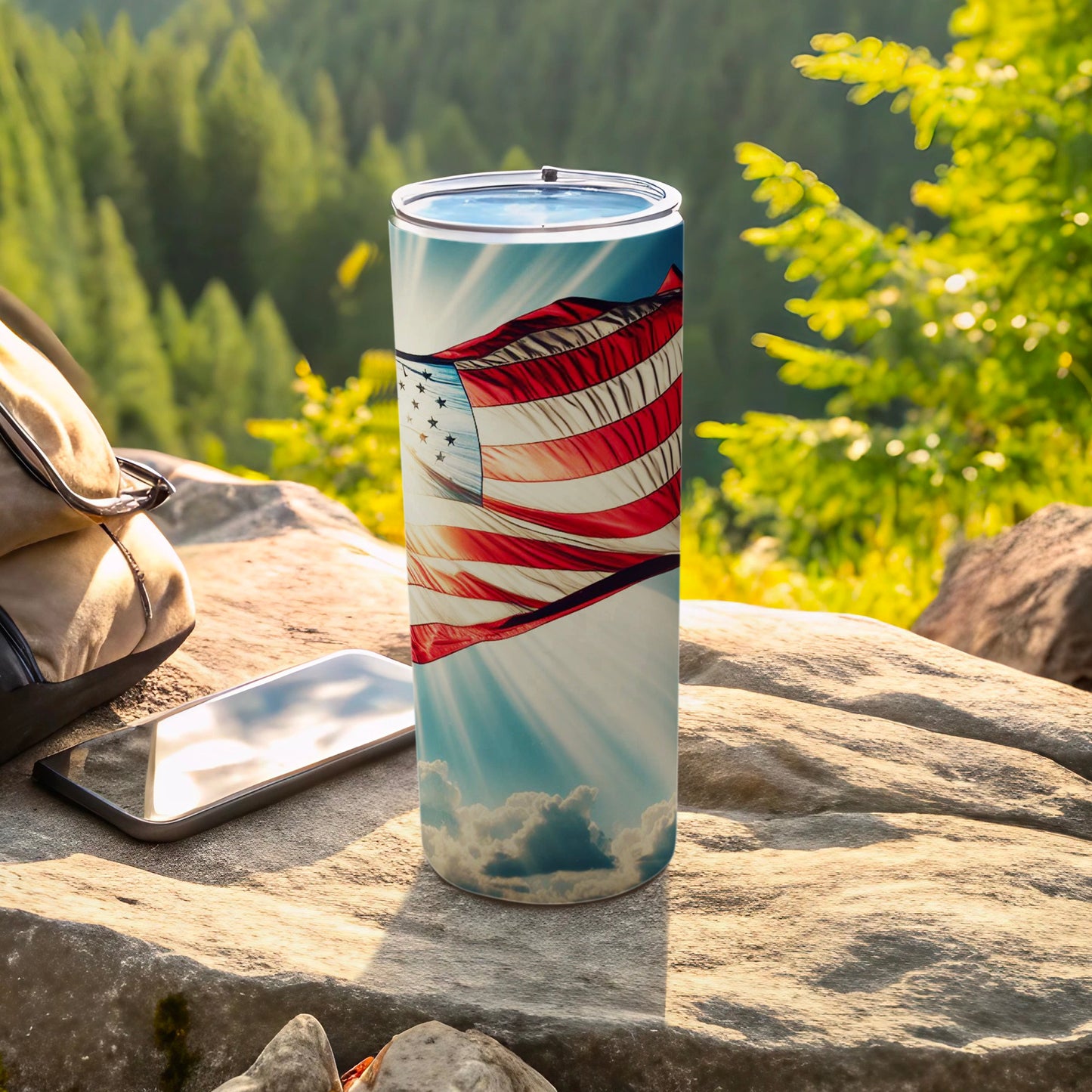 Patriotic tumbler with US flag design sits on rocks outdoors.