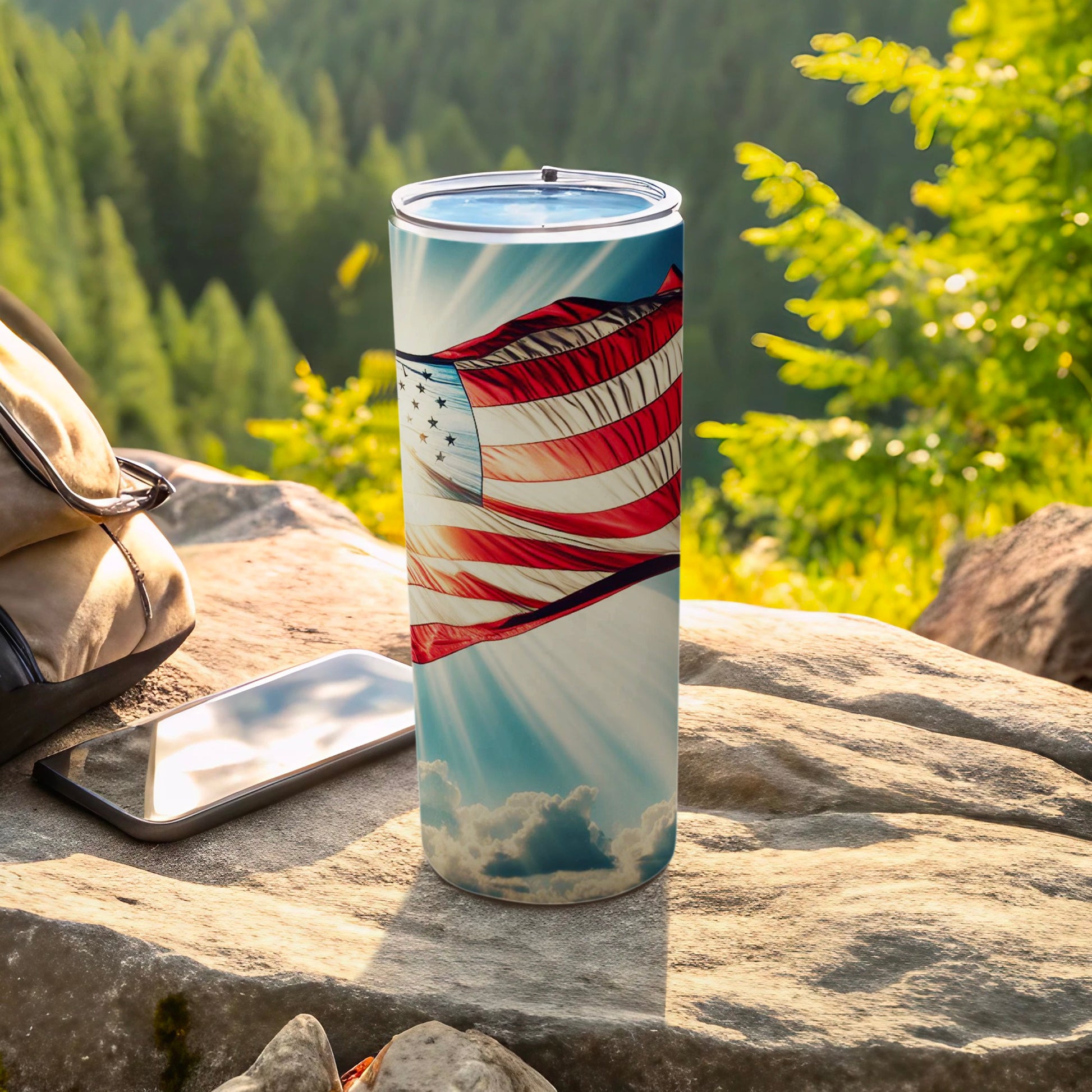 Patriotic tumbler with US flag design sits on rocks outdoors.