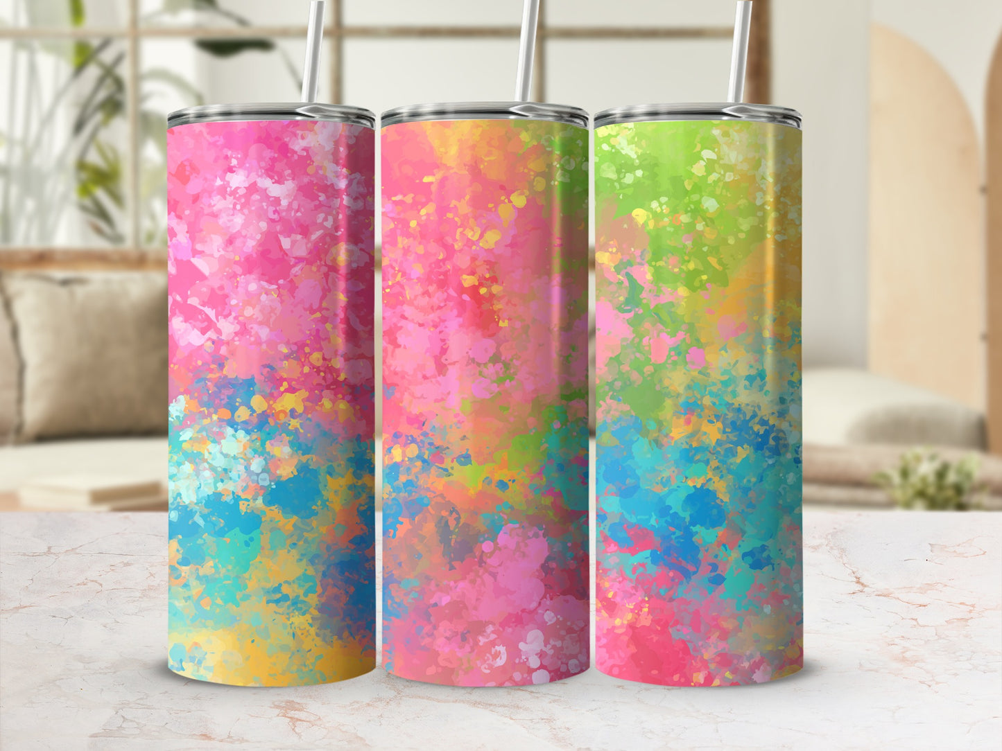 Three tumblers with colorful abstract splatter designs and straws on a marble surface.