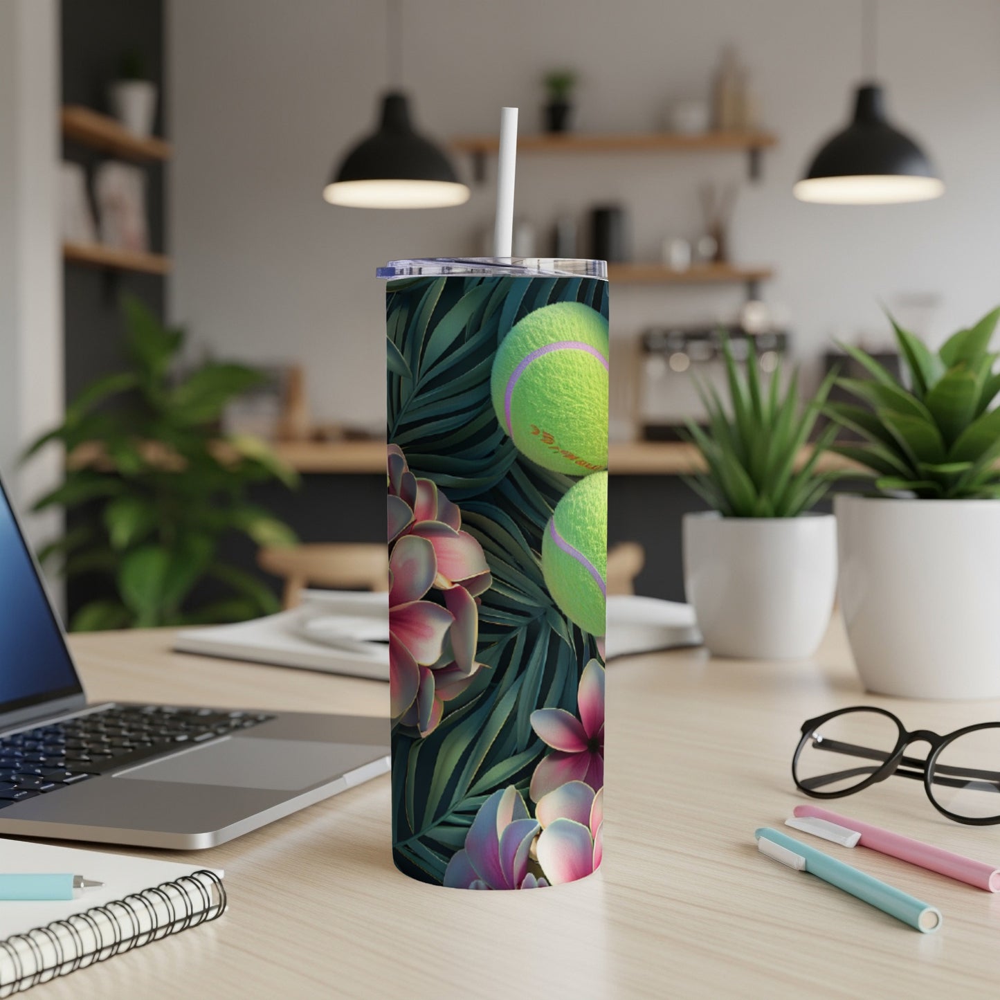 Tumbler with tennis balls and tropical leaves, resting on a desk.