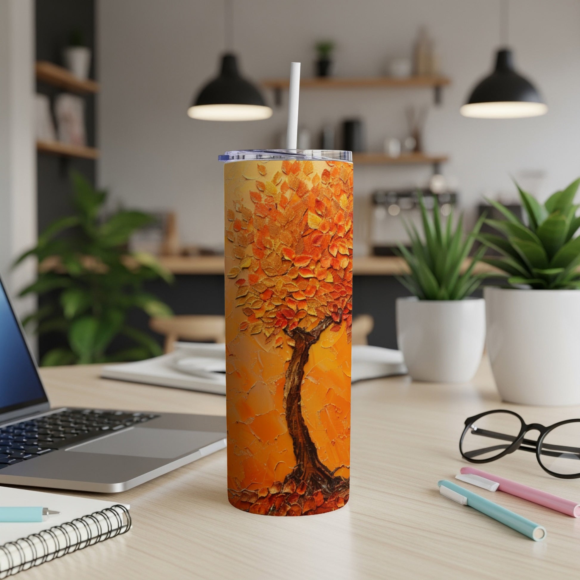 Orange abstract tree on a textured tumbler with a straw and desk background.