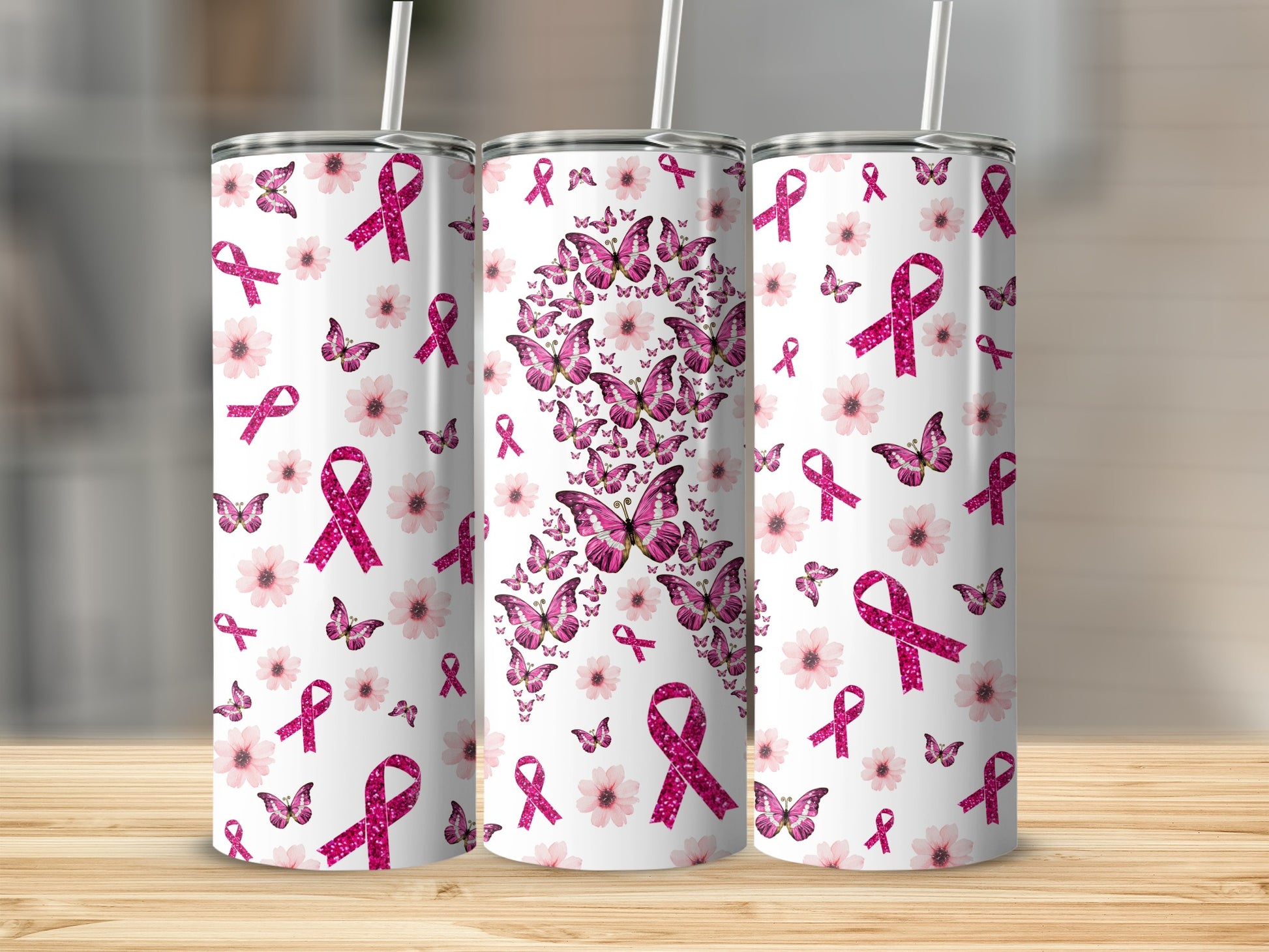 Three tumblers with pink ribbons and flowers design on a wooden surface.