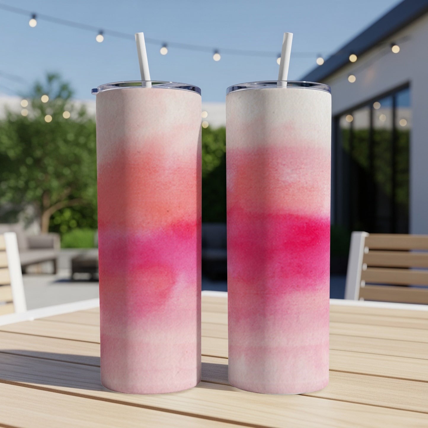 Two pink and white ombre tumblers with straws on a wooden table.