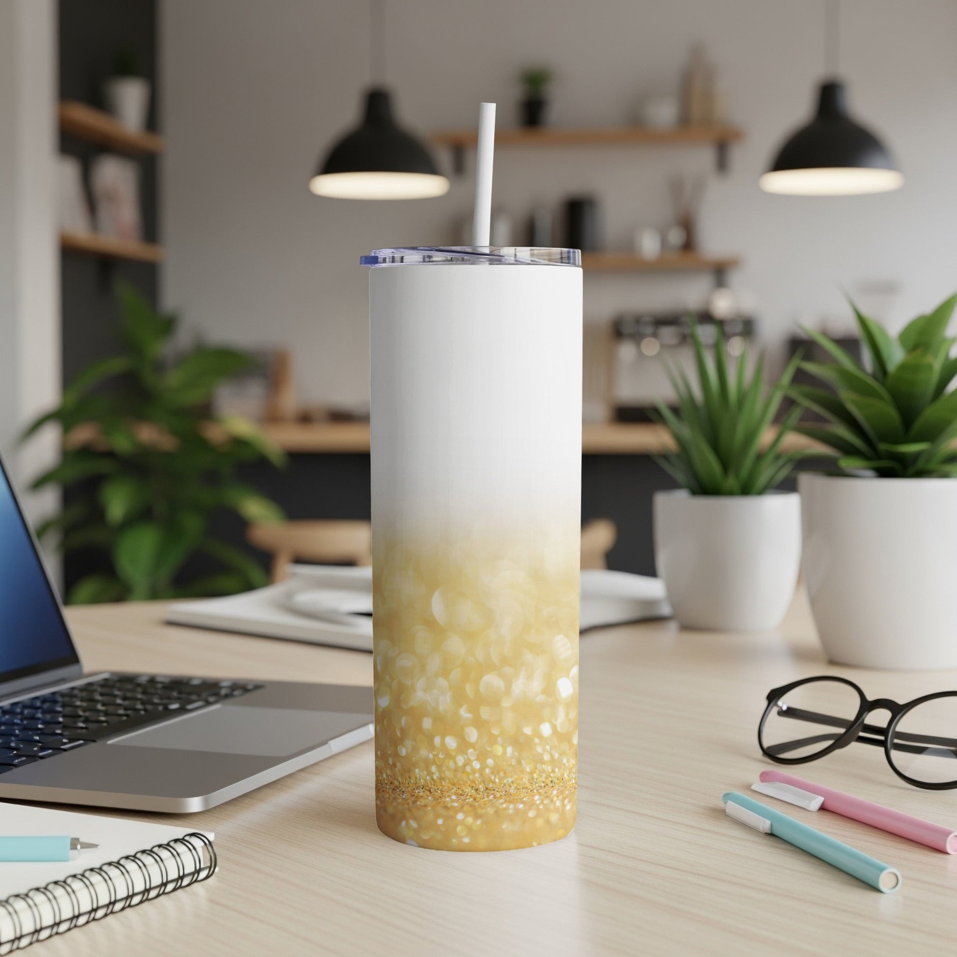 White and gold glitter tumbler with straw on desk next to laptop.