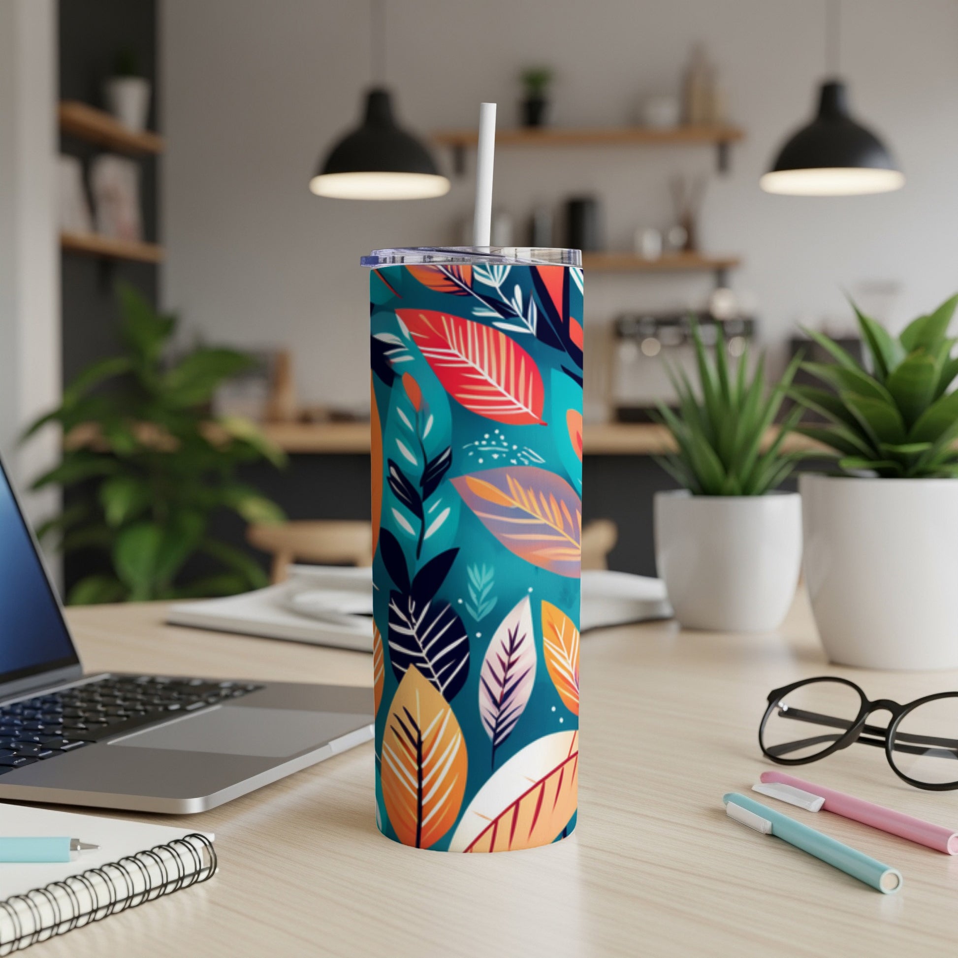 Teal skinny tumbler with colorful tropical leaf pattern and white straw.