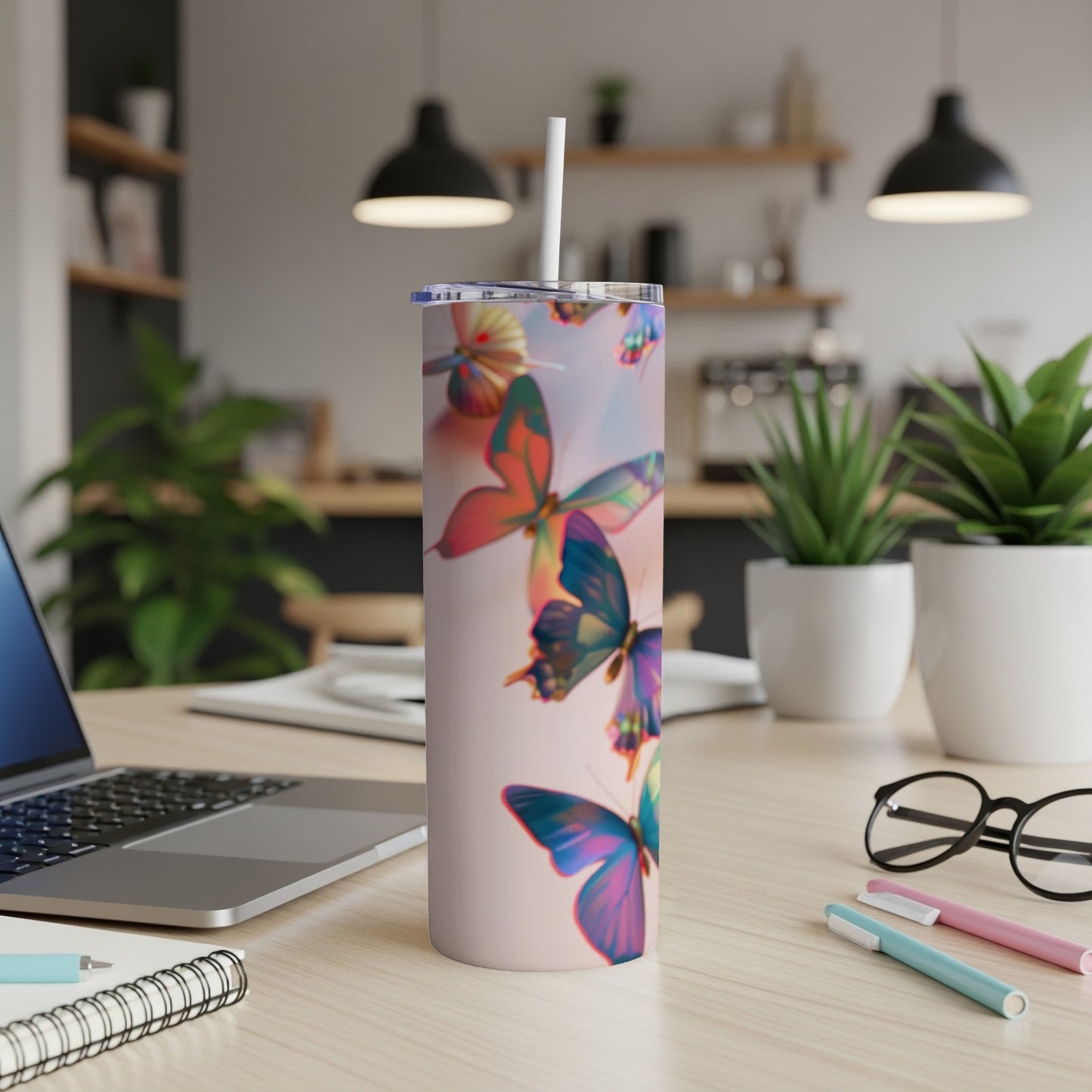 Pink tumbler with colorful butterflies, straw, and office desk background.