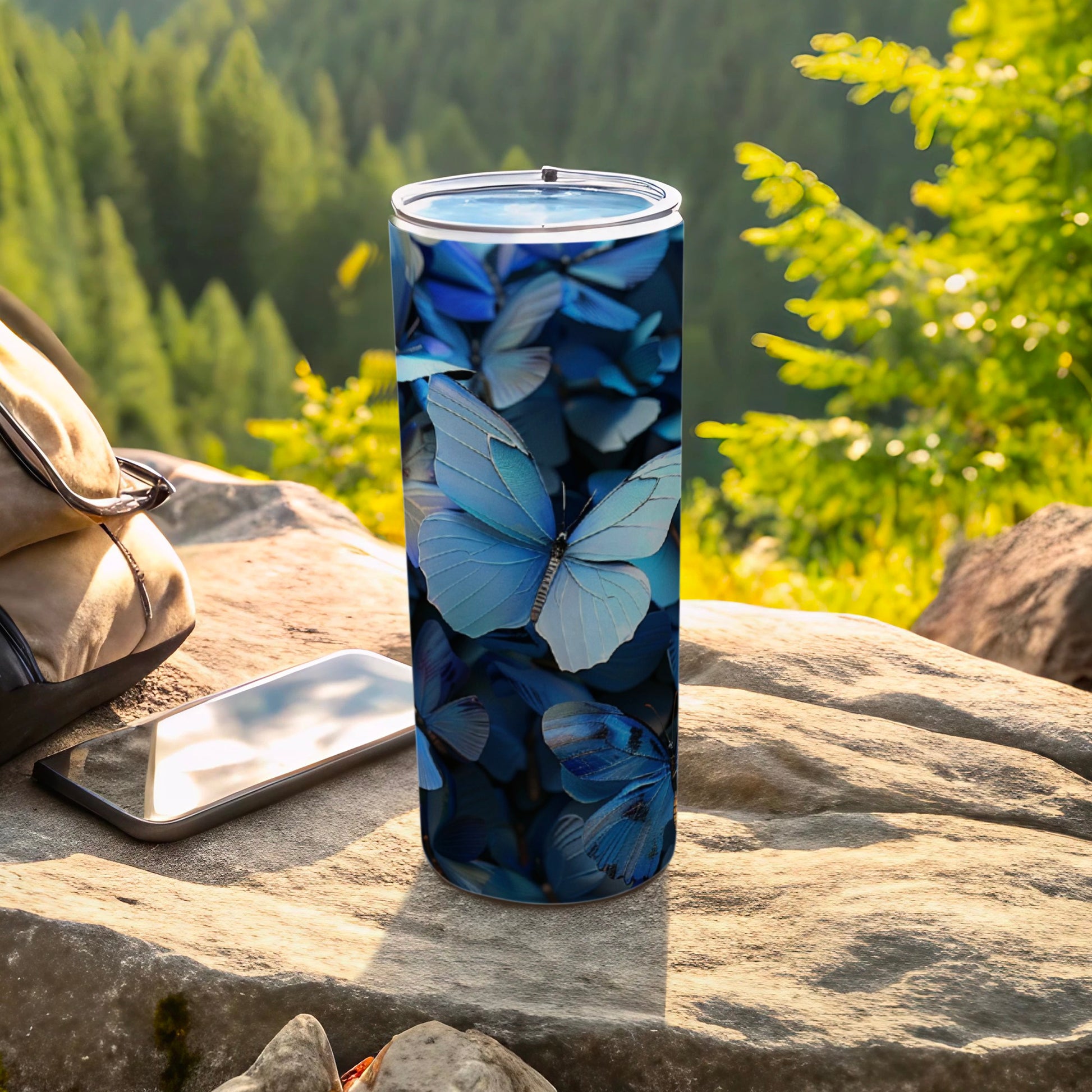 Blue butterflies adorn a silver travel tumbler on a rock.