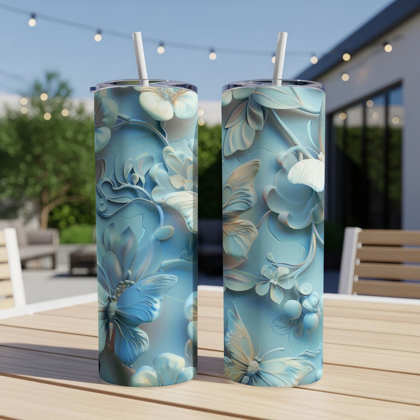 Two blue floral and butterfly patterned tumblers with straws on a wooden table.