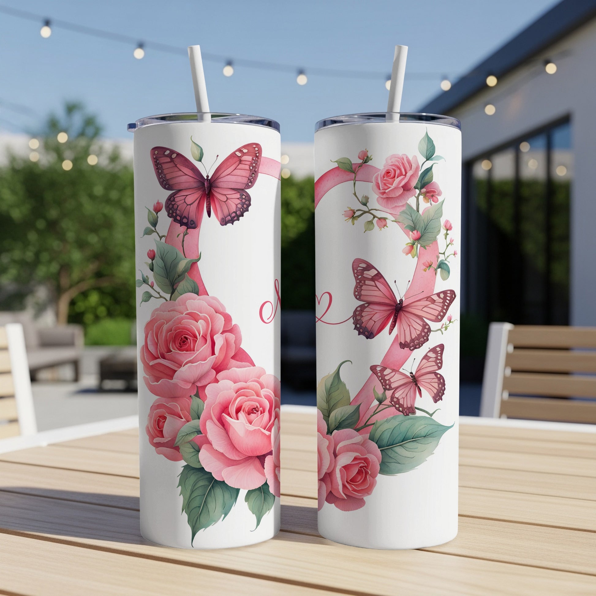 Two pink butterfly and rose themed tumblers with straws on a table.