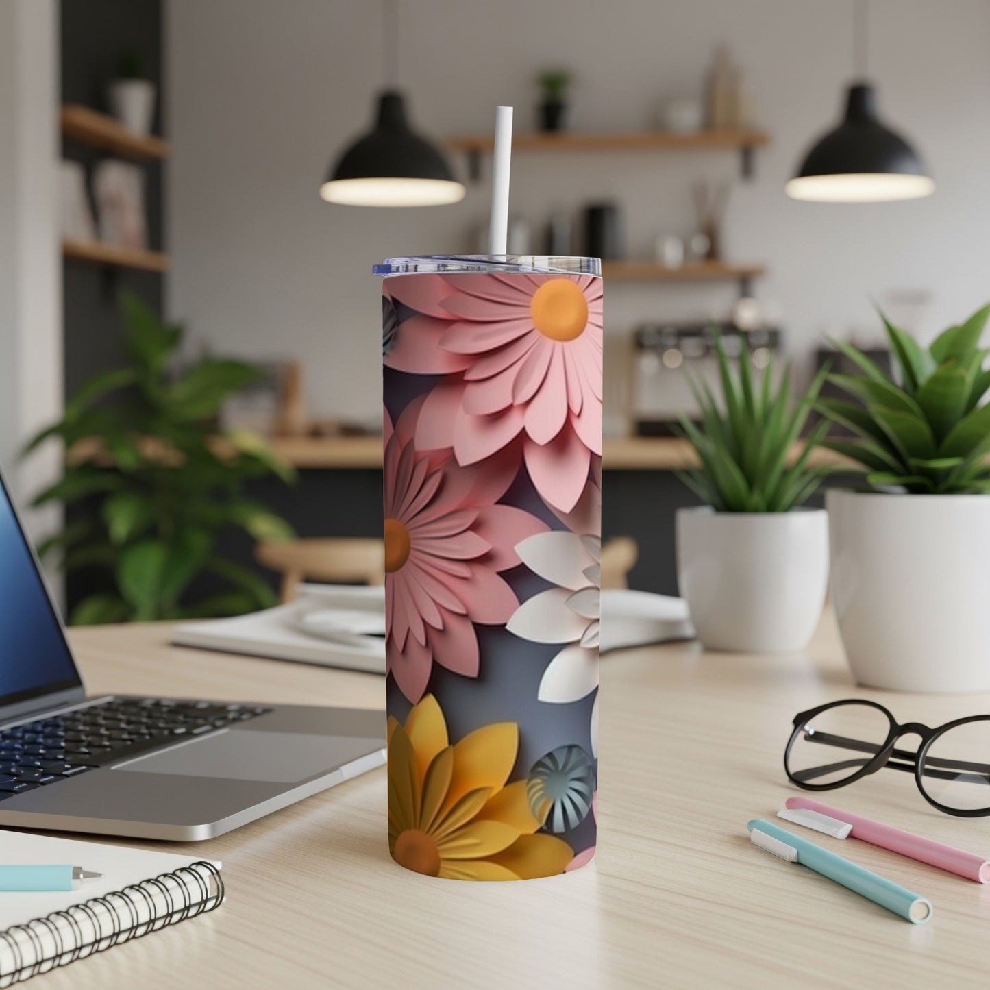 Pink and yellow paper flowers adorn a white skinny tumbler on a desk.