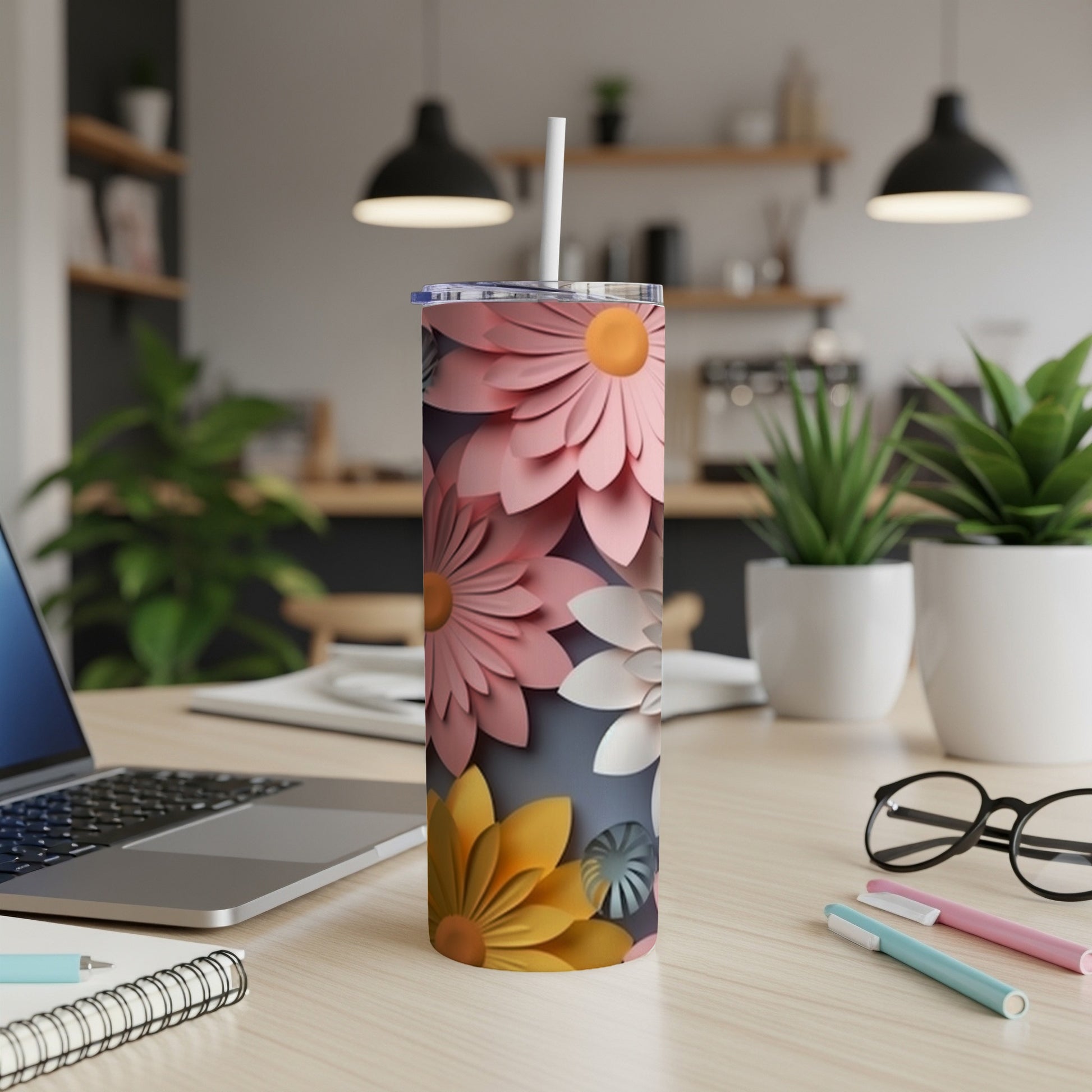 Pink and yellow paper flowers adorn a white skinny tumbler on a desk.