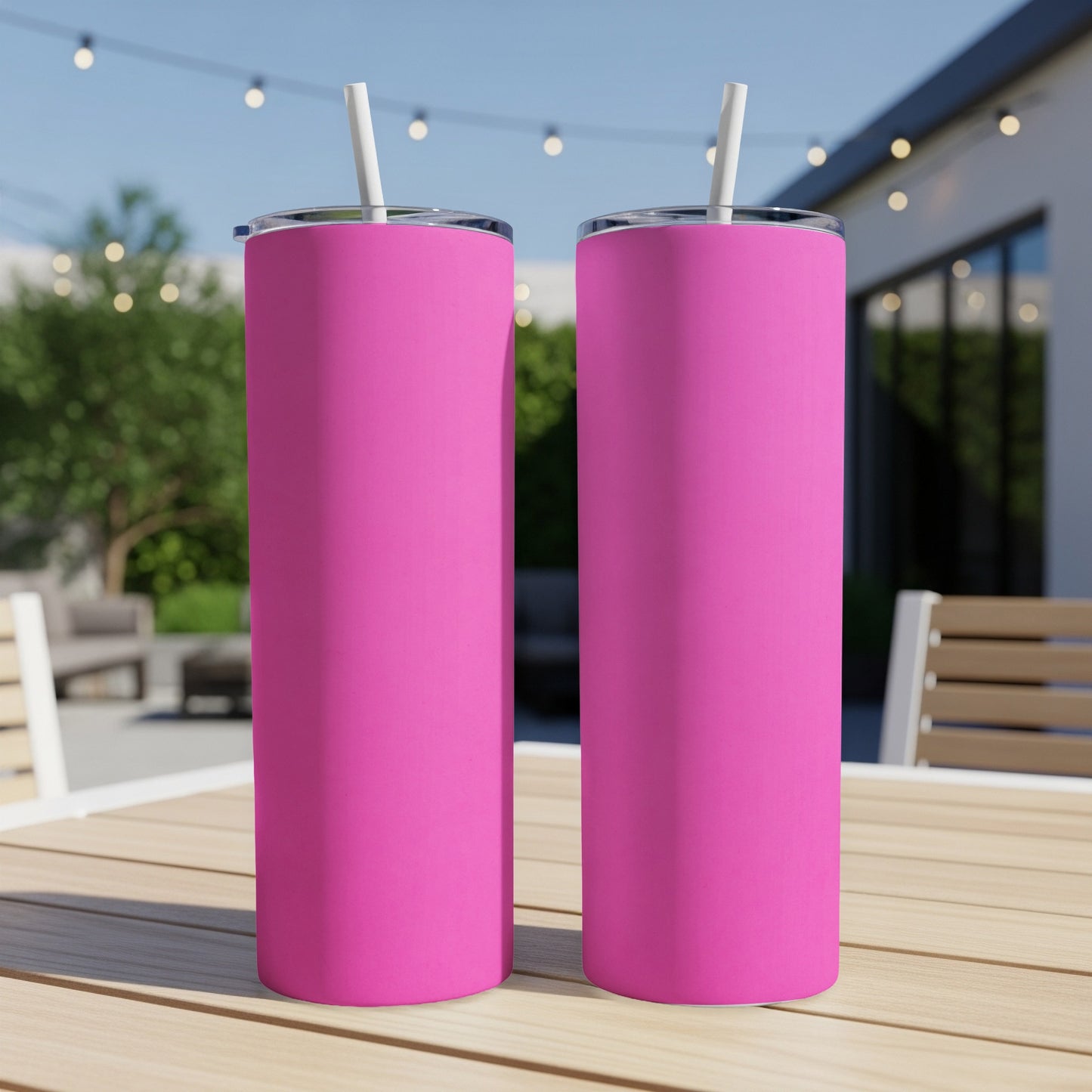 Two bright pink tumblers with straws on a wooden table outdoors.