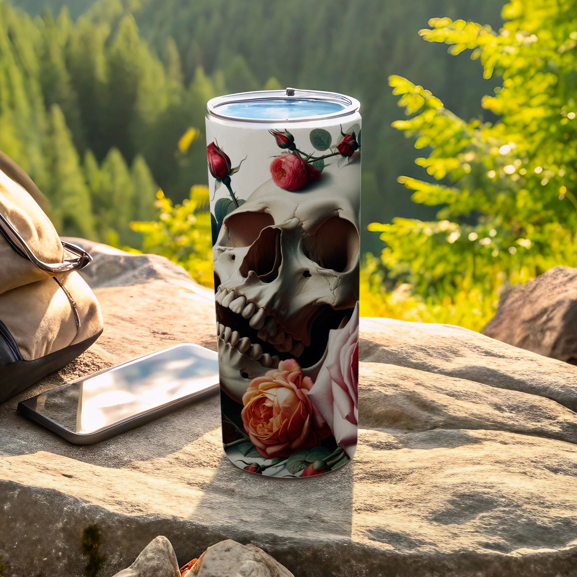 Skull and rose design on a stainless steel tumbler with smartphone and bag.