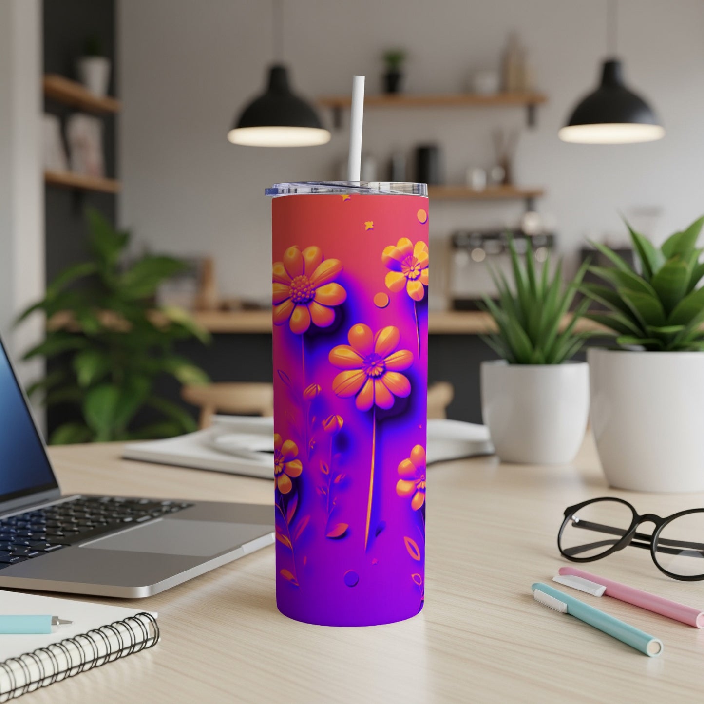 Purple and orange tumbler with yellow flowers and a straw, on a desk.