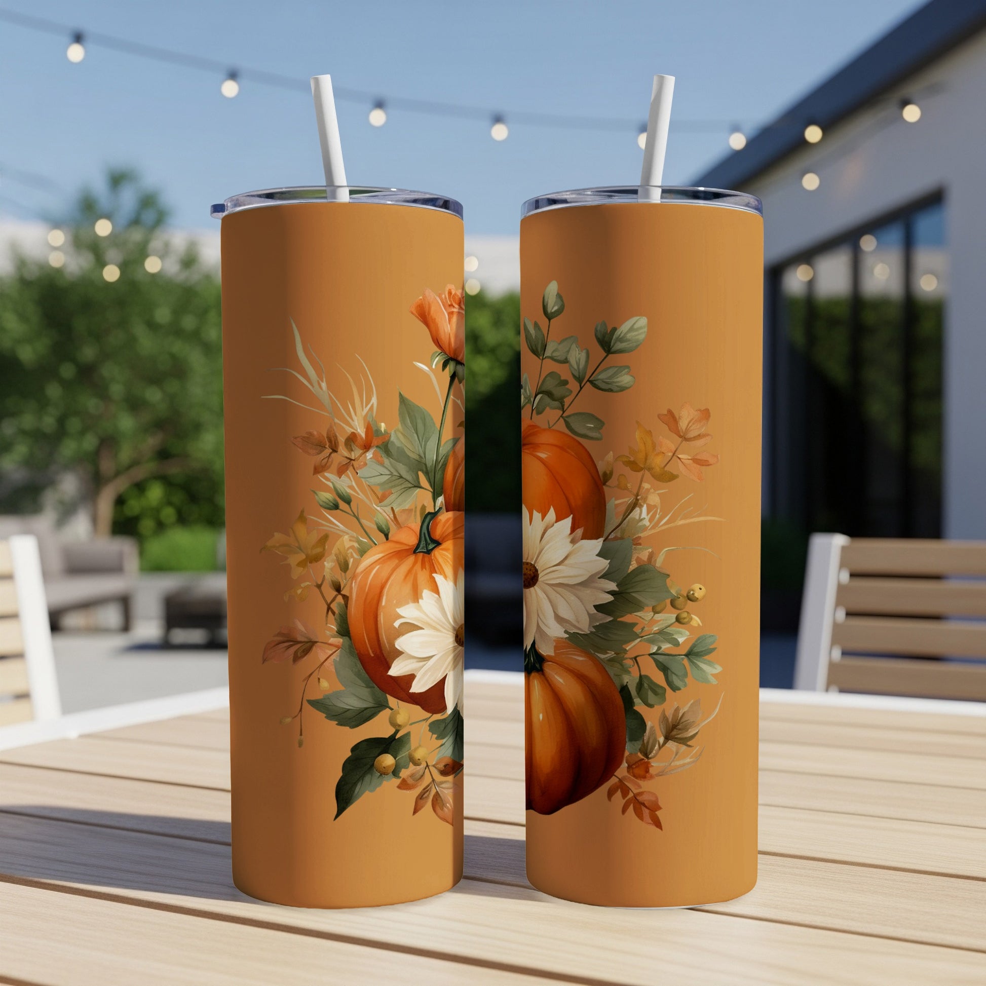 Two tumblers with a pumpkin and floral design sit on a table outdoors.