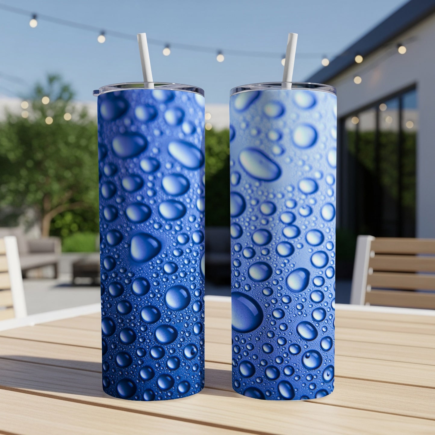 Two blue tumblers with water droplet design and straws on a table.