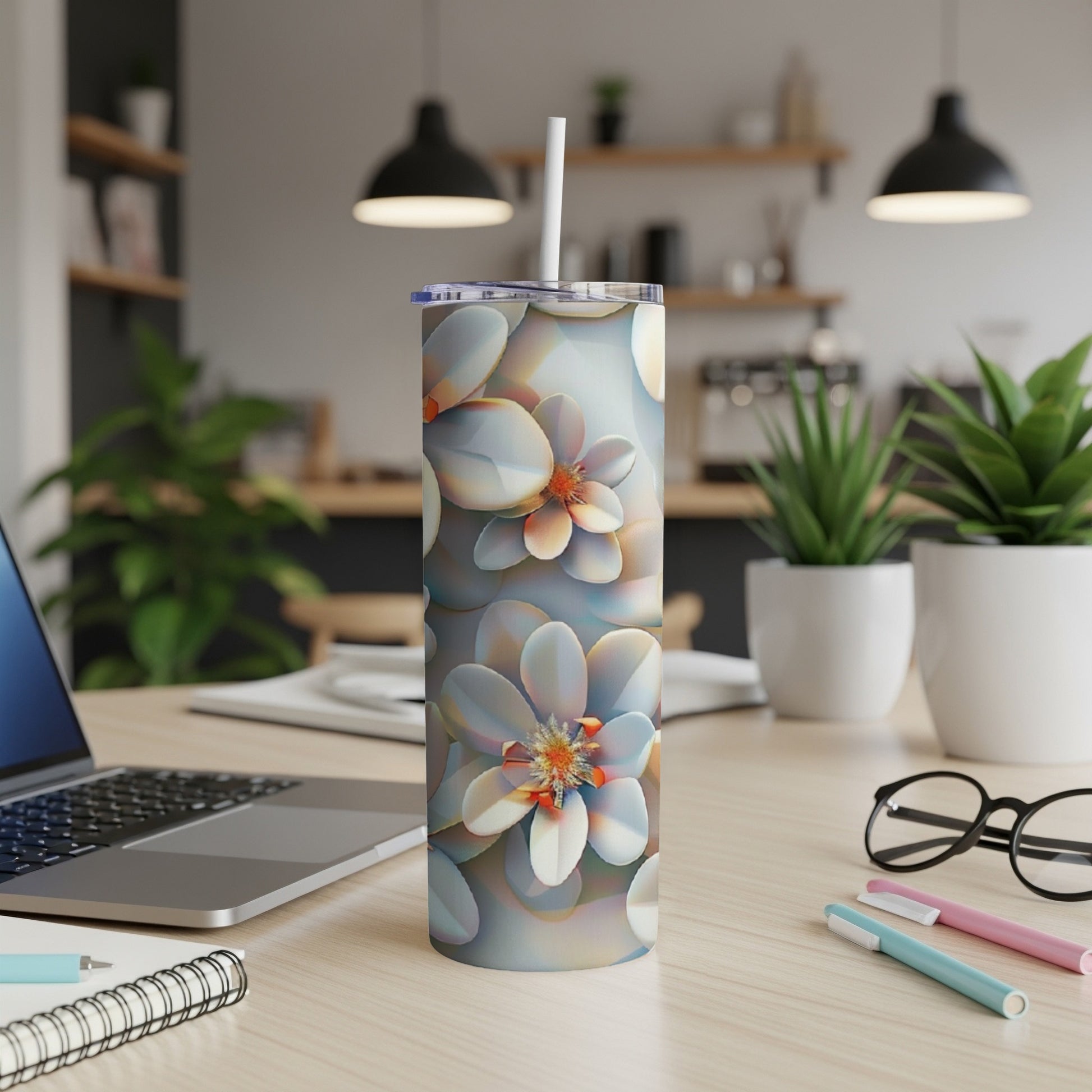 Floral patterned tumbler with a straw on a desk with a laptop and pens.