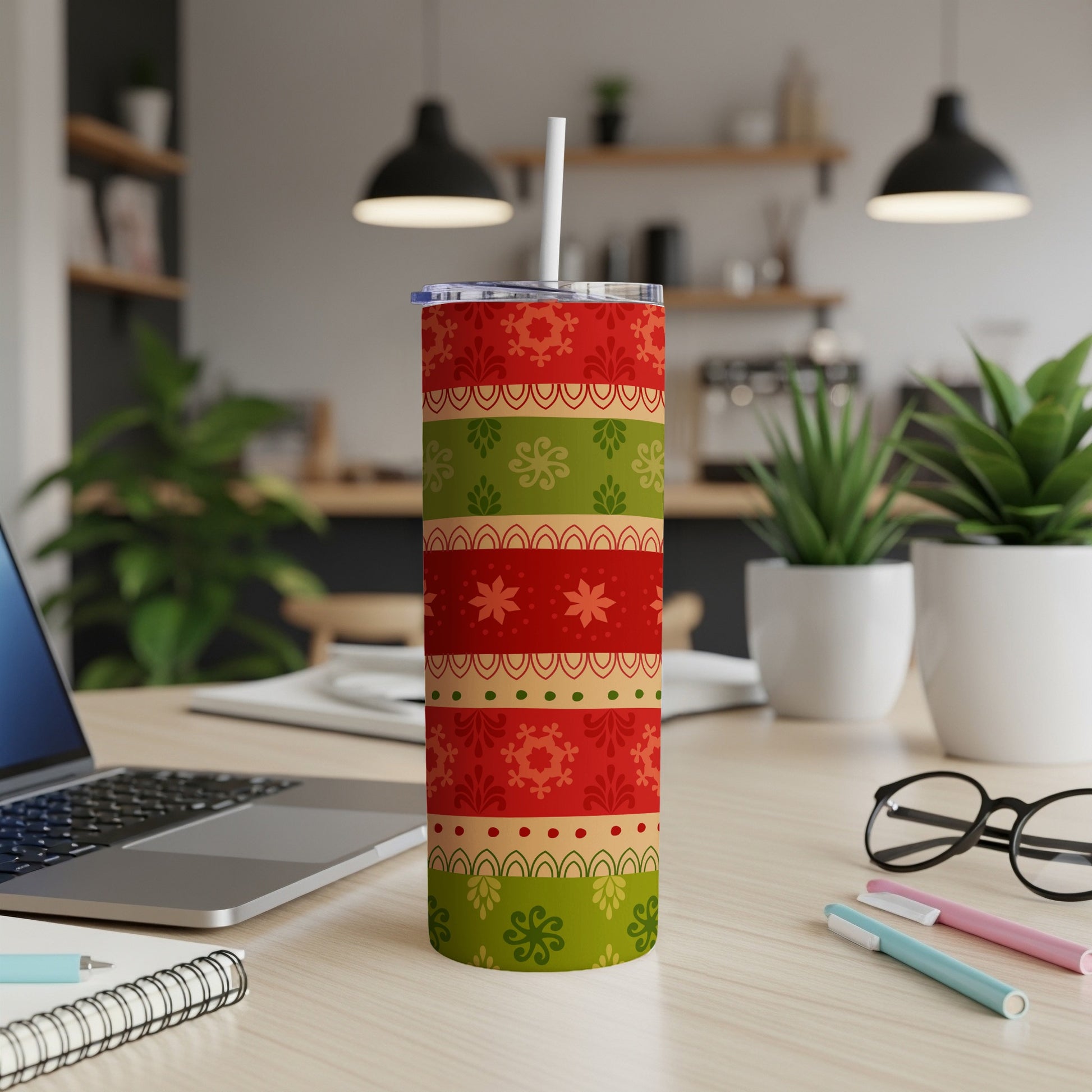 Red, green, and gold striped Christmas tumbler with straw on a desk.