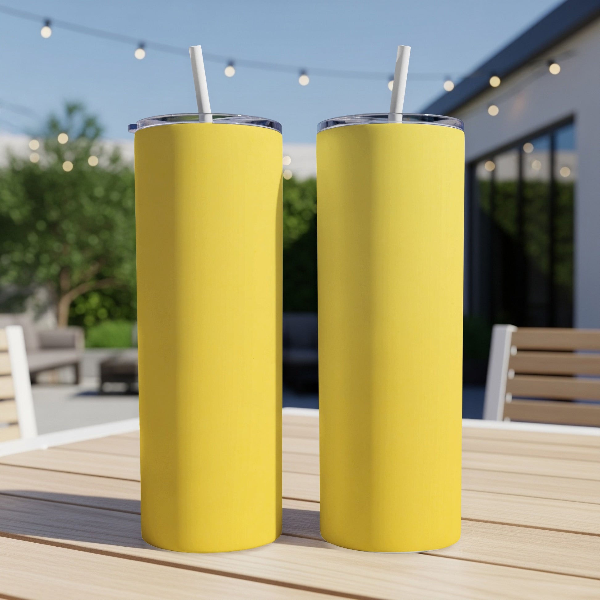 Two yellow tumblers with straws sit on a wooden table outdoors.