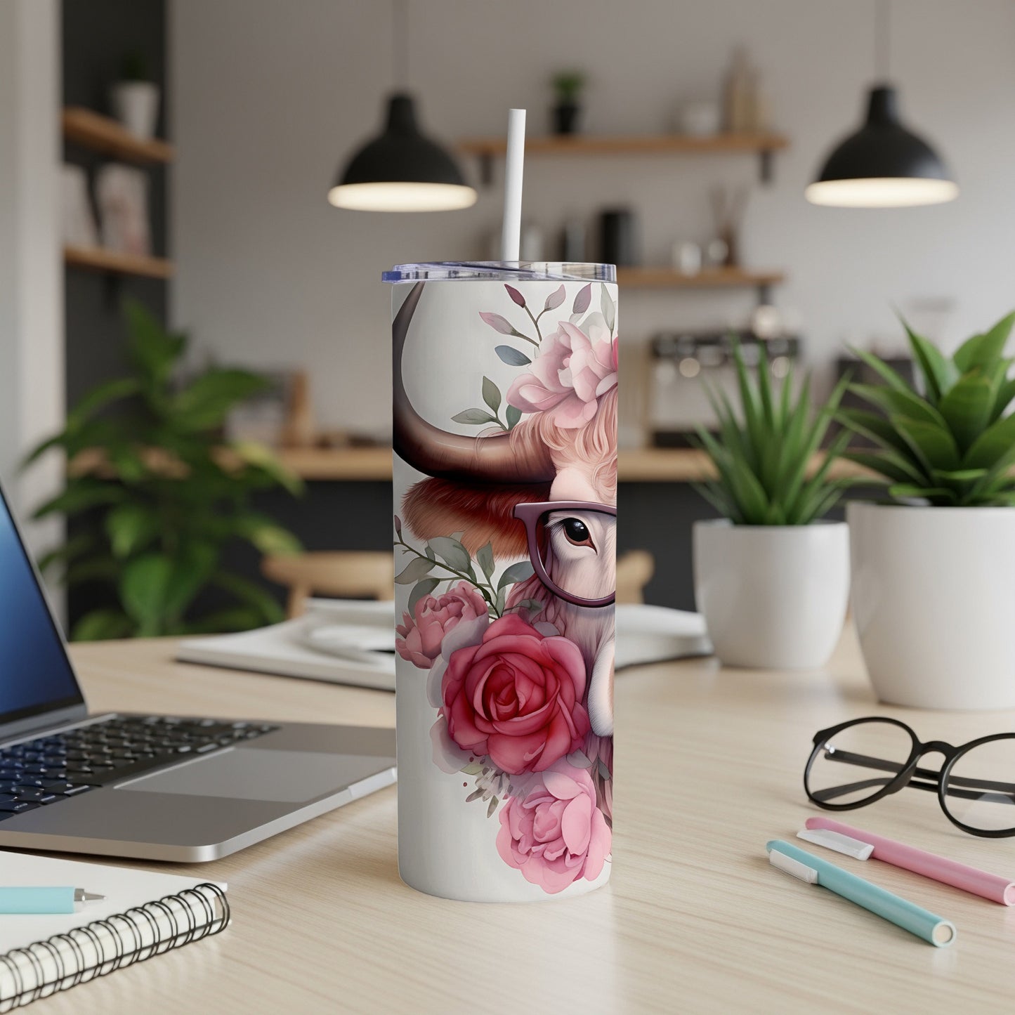 Cow with glasses and roses on a tumbler, with a laptop and pens in the background.