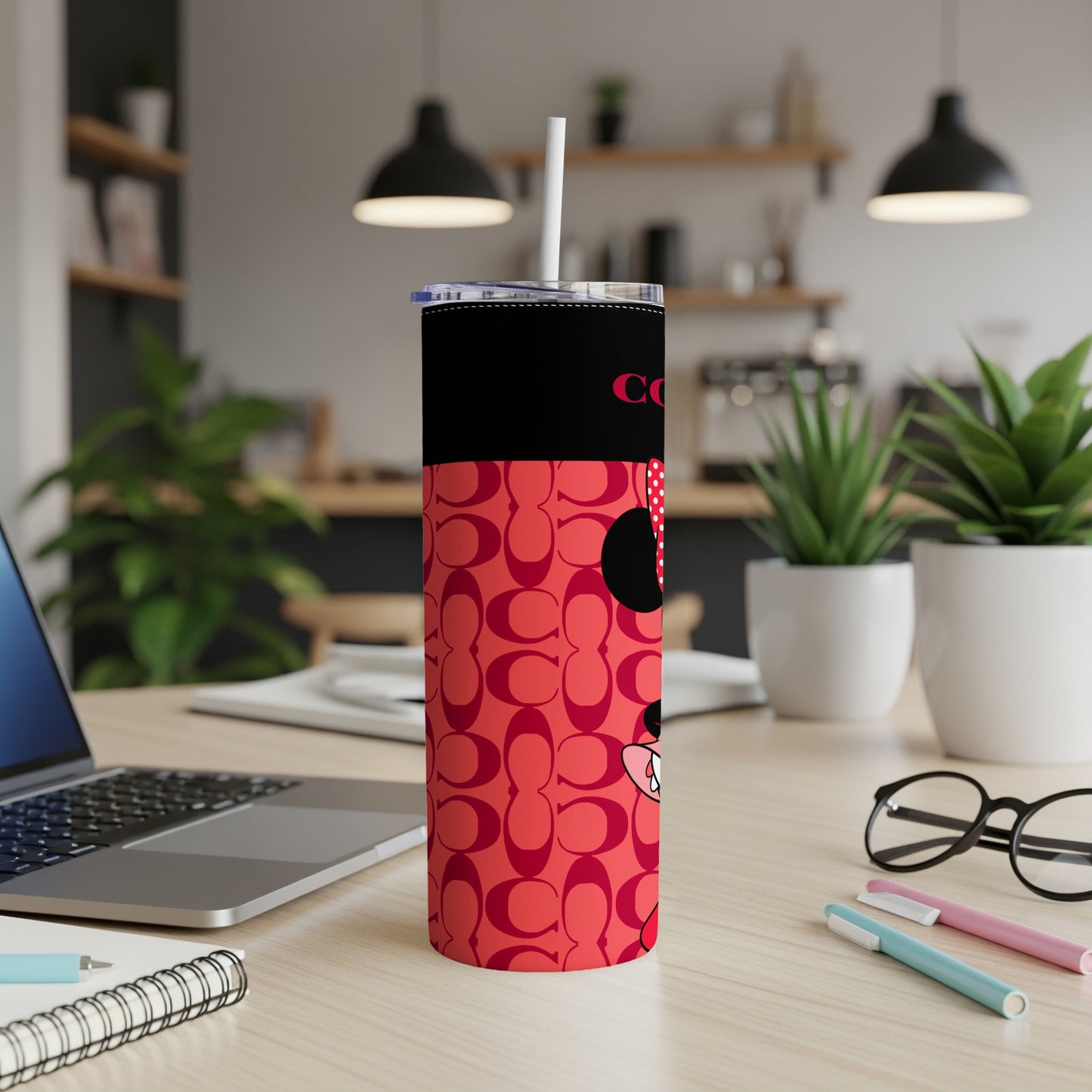 Red tumbler with COACH pattern and Minnie Mouse, on a desk.