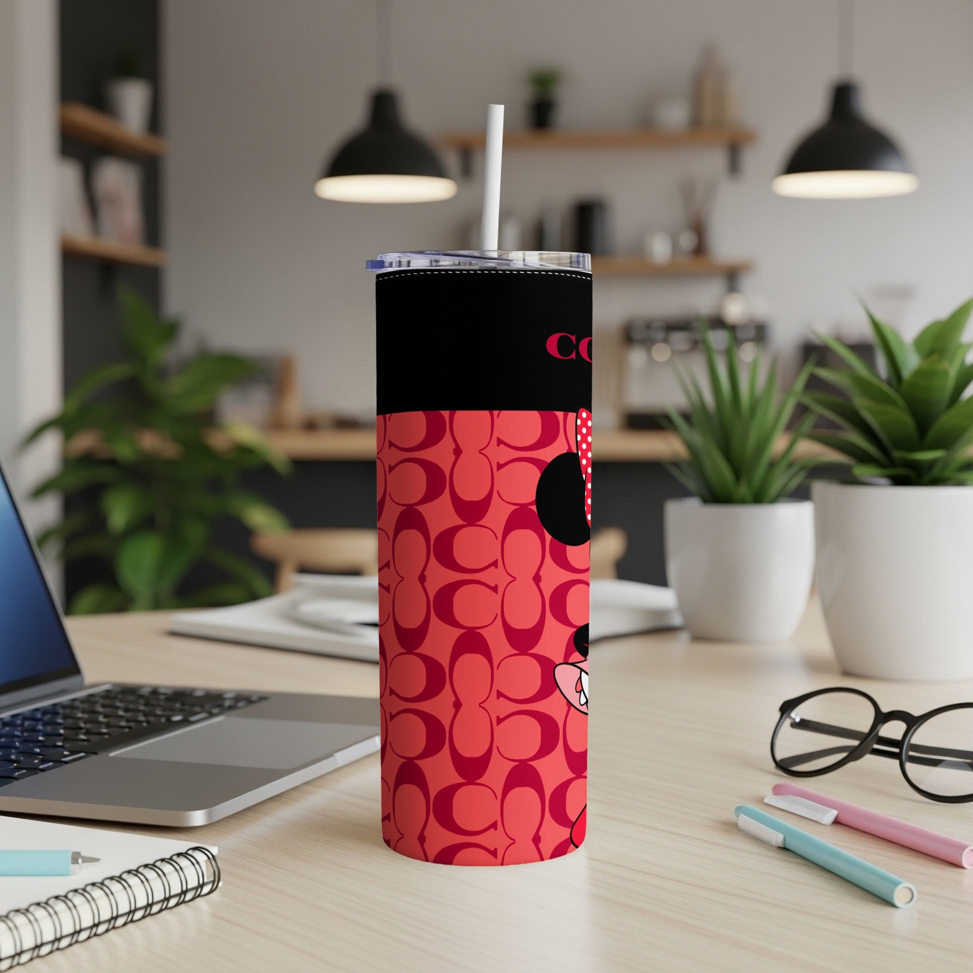 Red tumbler with COACH pattern and Minnie Mouse, on a desk.