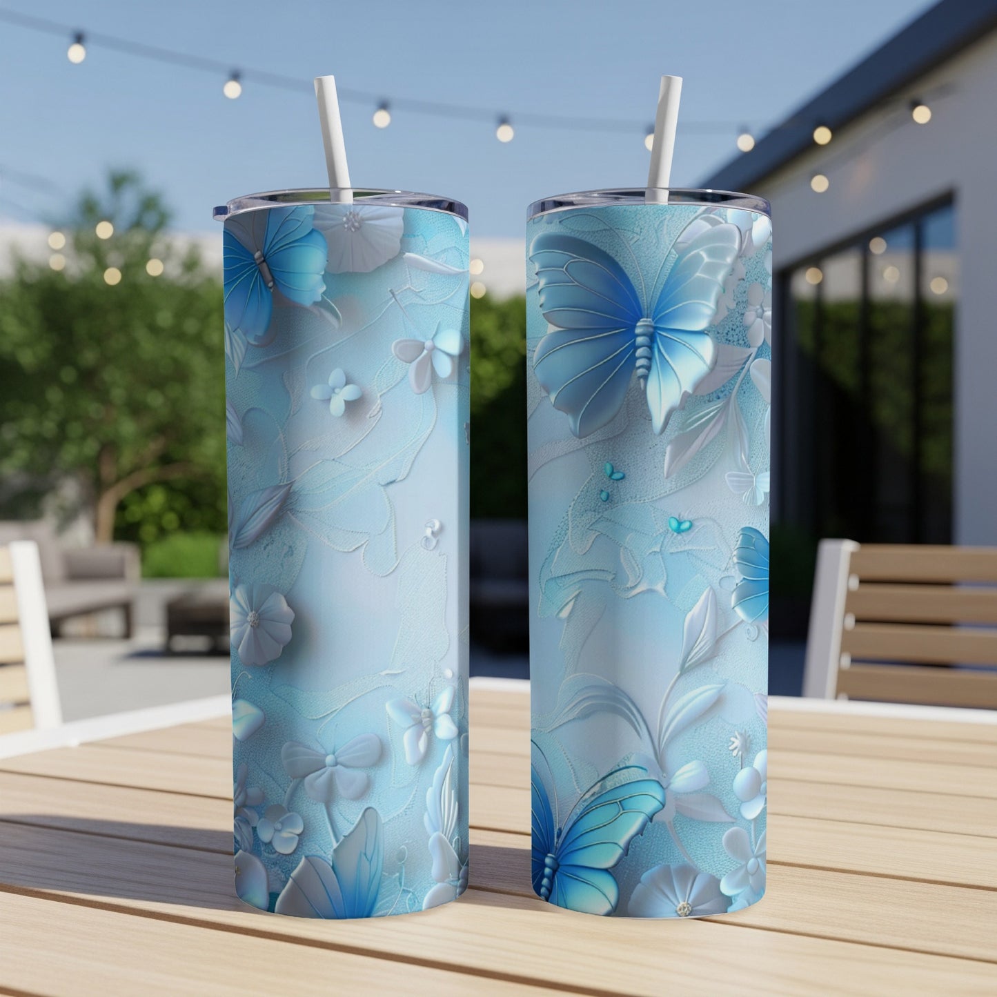 Two light blue tumblers with butterfly and floral embossed designs on an outdoor table.