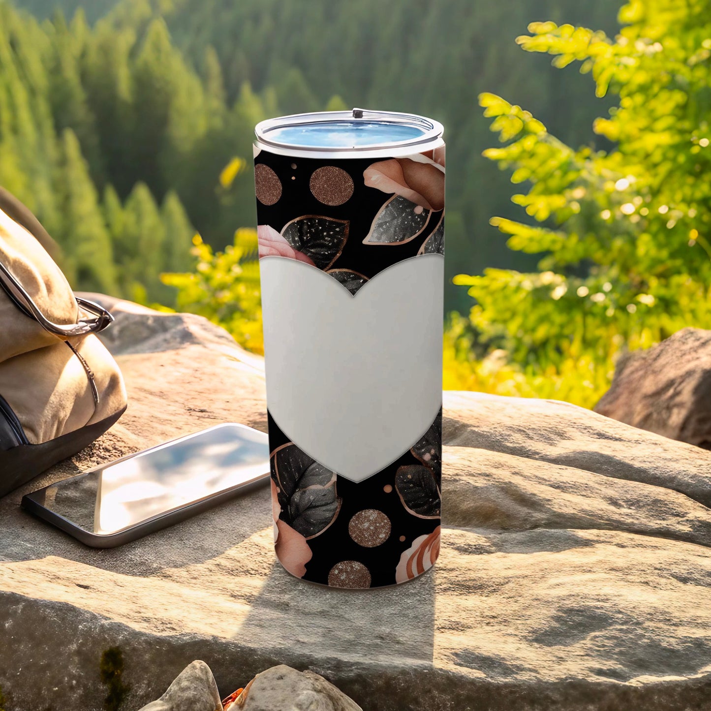 Black speckled tumbler with white heart design on rocky outdoor surface.