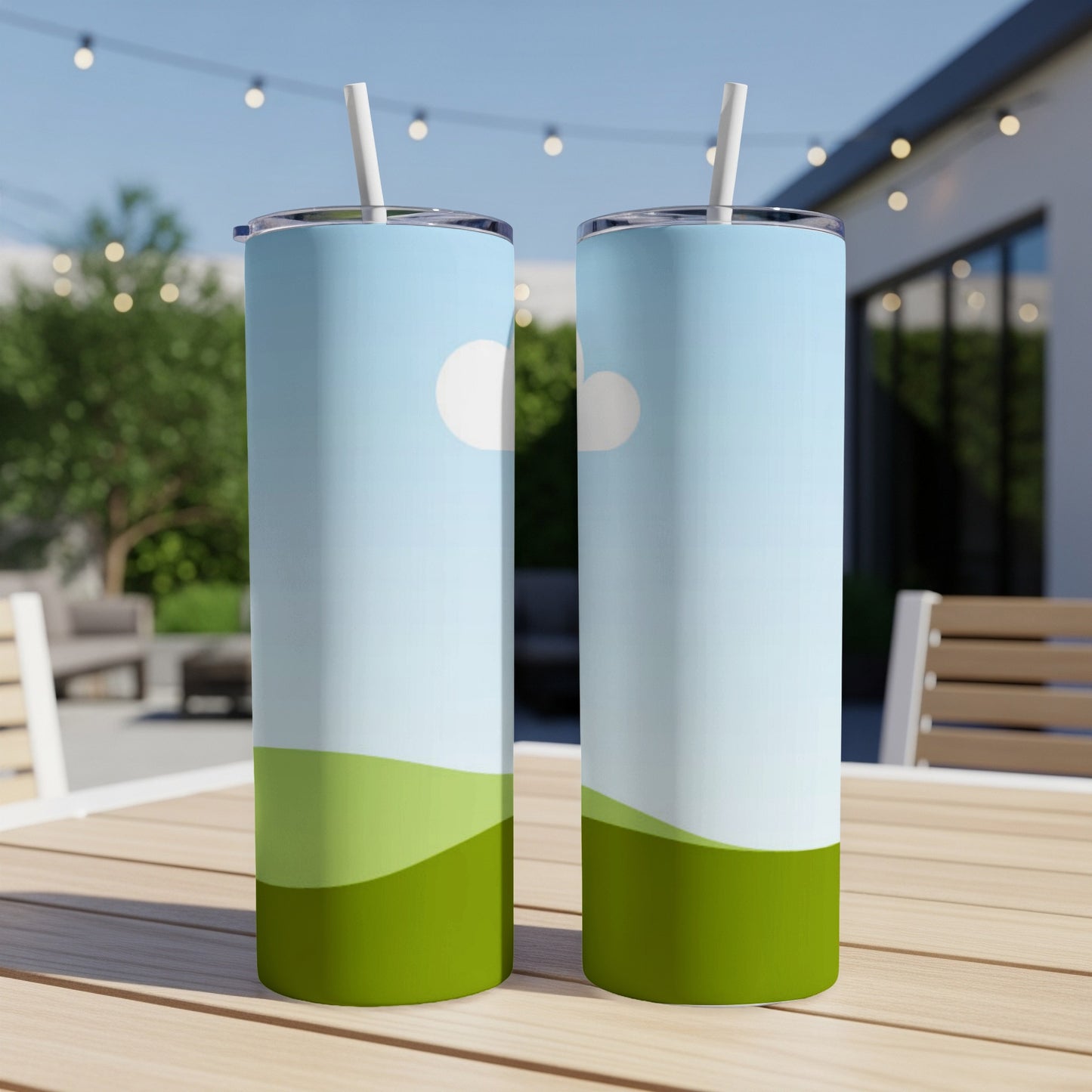 Two tall tumblers with a rolling green hill and sky design sit on a table.