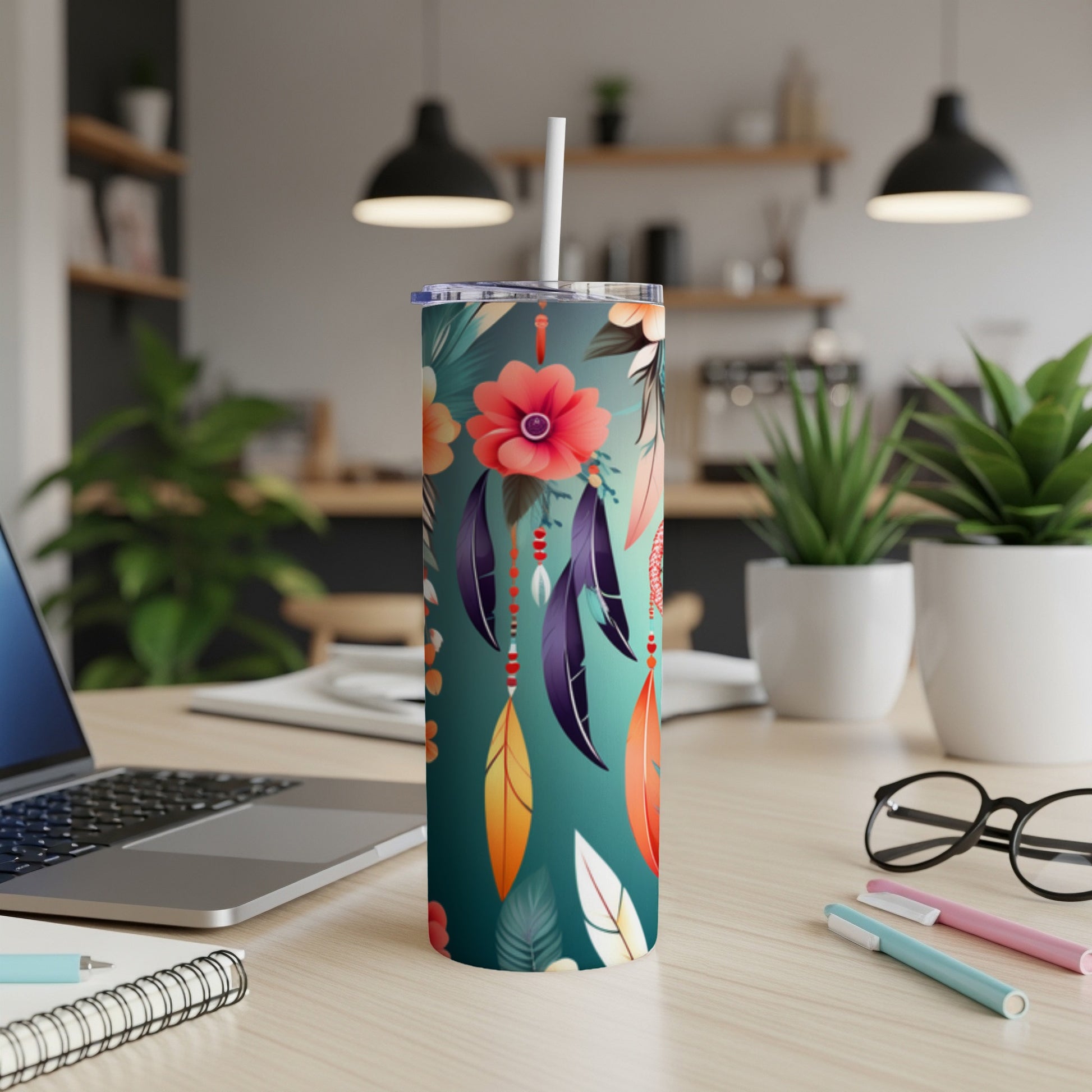 Floral patterned tumbler with feathers and straw on desk.