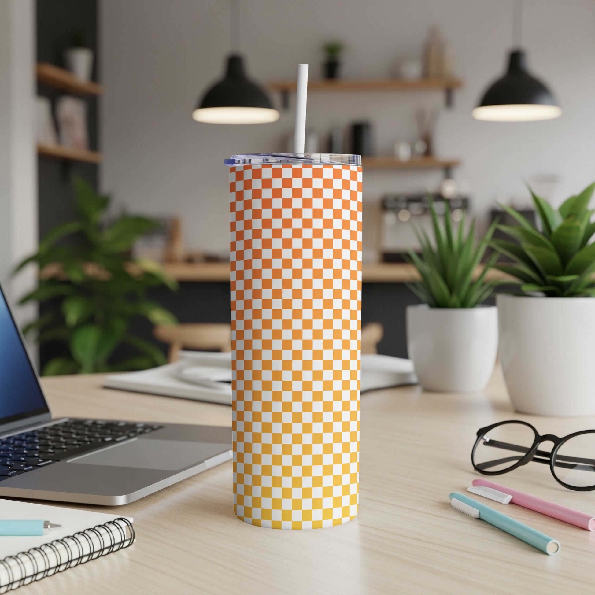 Orange and white checkered tumbler with a straw on a desk.