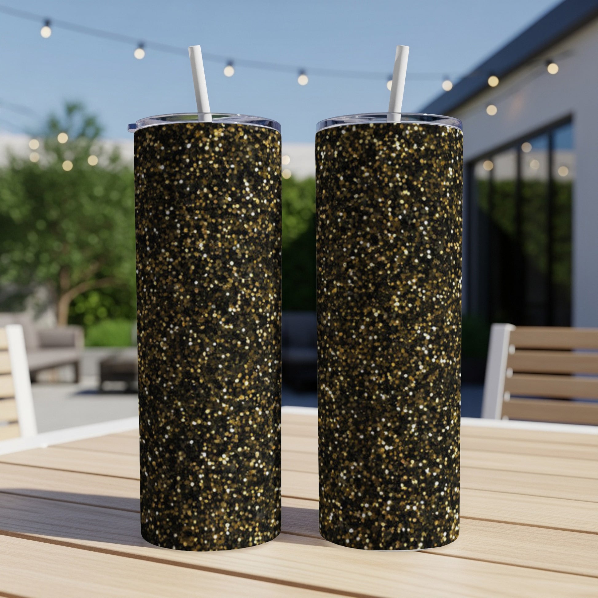 Two tall tumblers with black and gold glitter pattern, on an outdoor table.