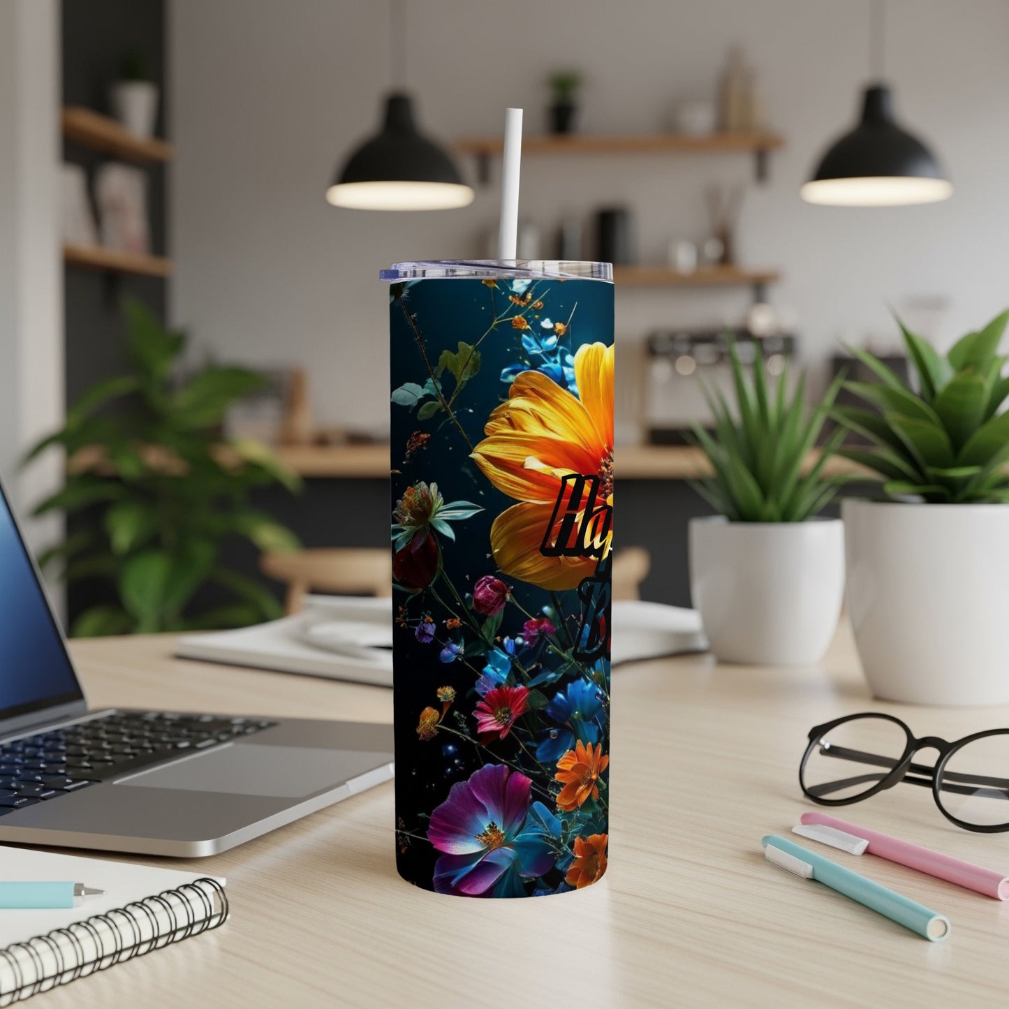 Tall tumbler with colorful floral design and white straw on a desk.