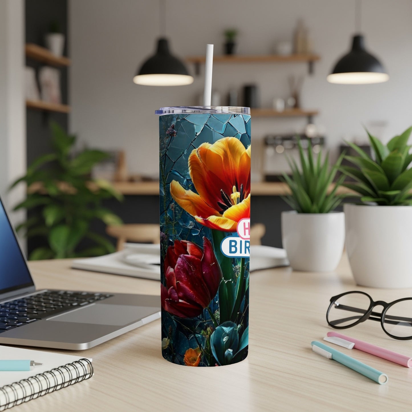 Floral tumbler with "Happy Birthday" text, on a desk with laptop and pens.