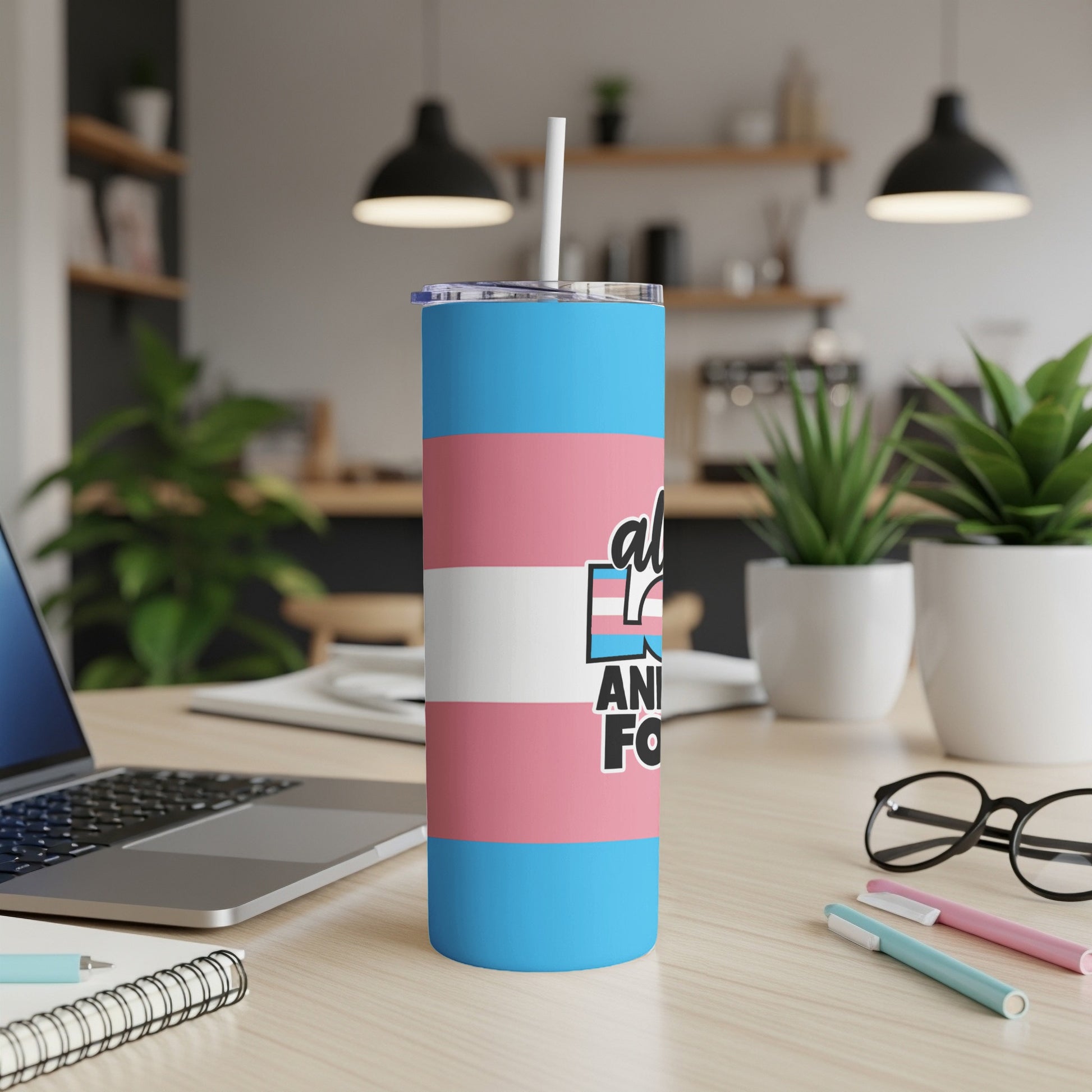 Transgender pride flag tumbler on a desk with a laptop and pens.