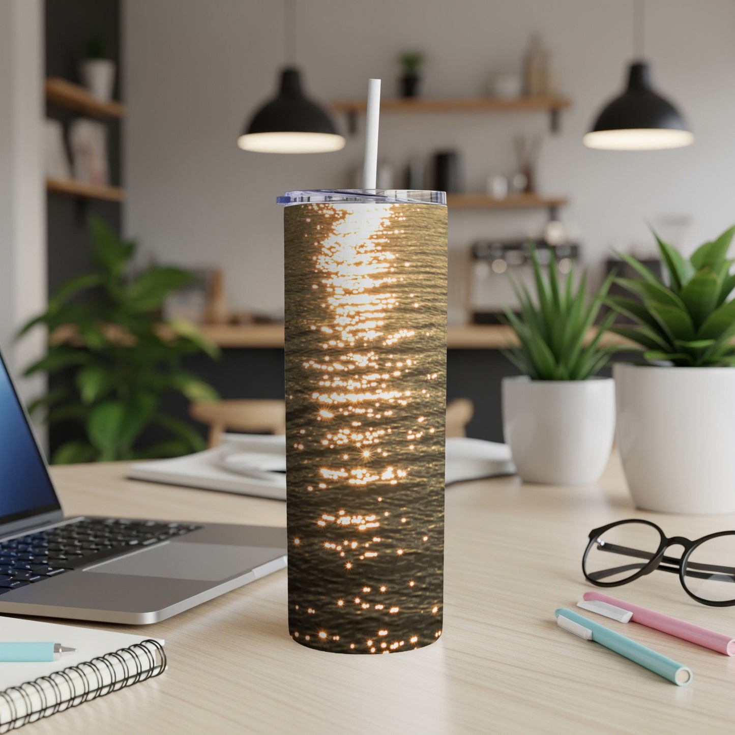 Tumbler with rippling water reflection design, on a desk with laptop and pens.