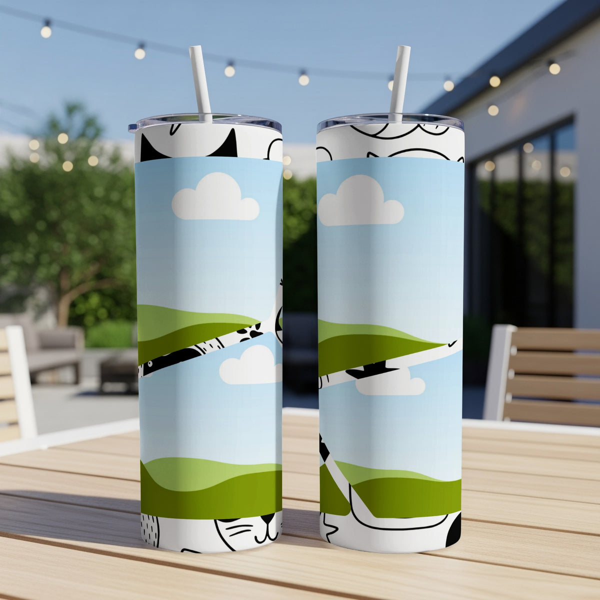 Two tumblers with a cartoon cat and landscape design on a wooden table.