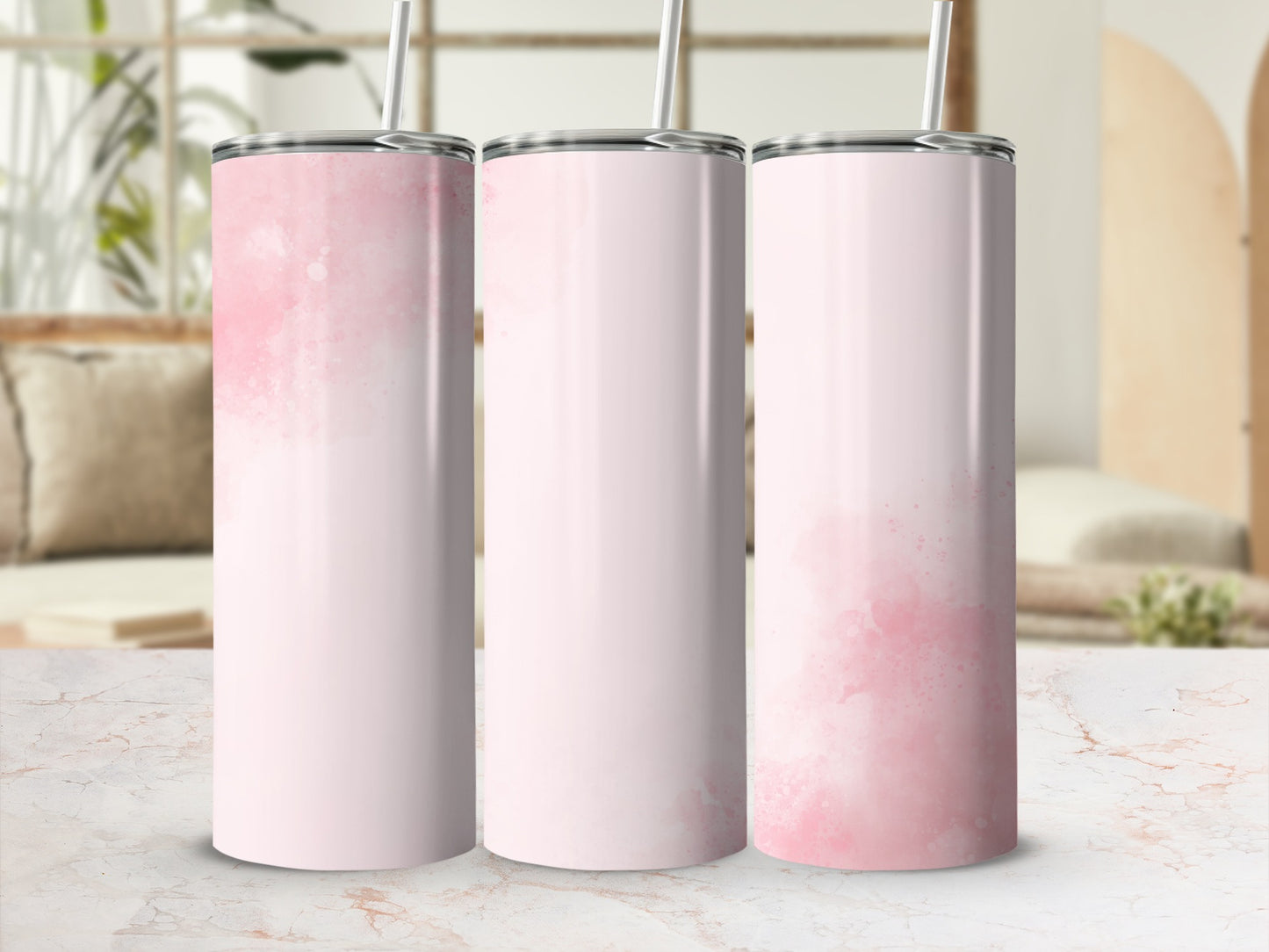 Three pink watercolor-patterned tumblers with straws on a marble surface.