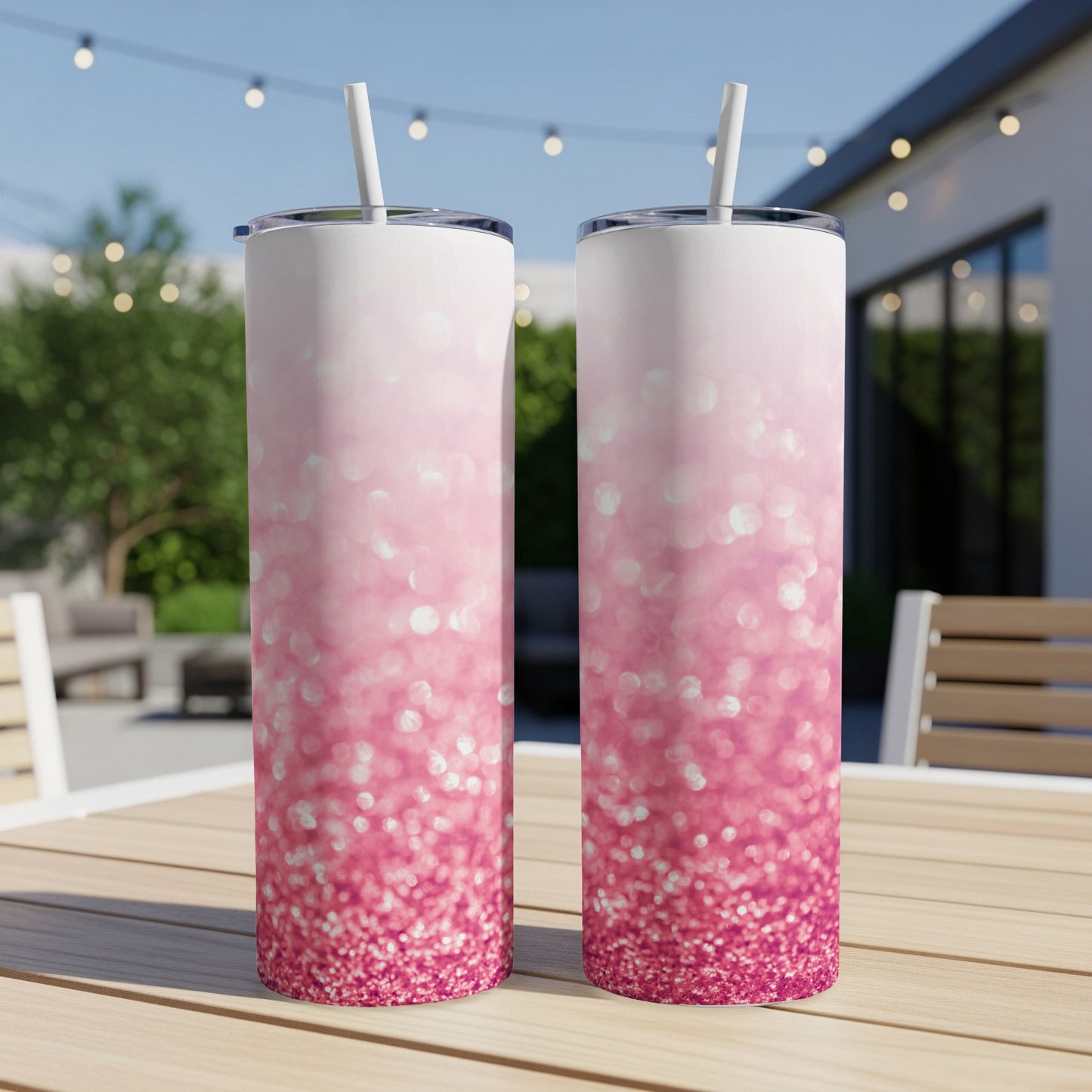 Two pink glitter ombre tumblers with straws on a wooden table outdoors.