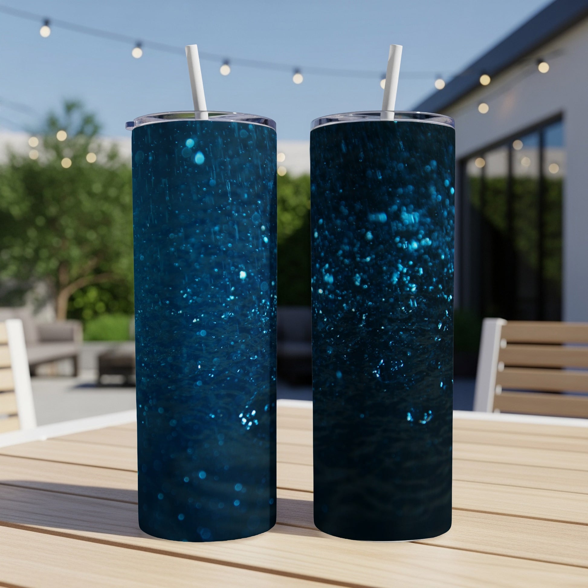 Two dark blue glitter tumblers with straws on a table.
