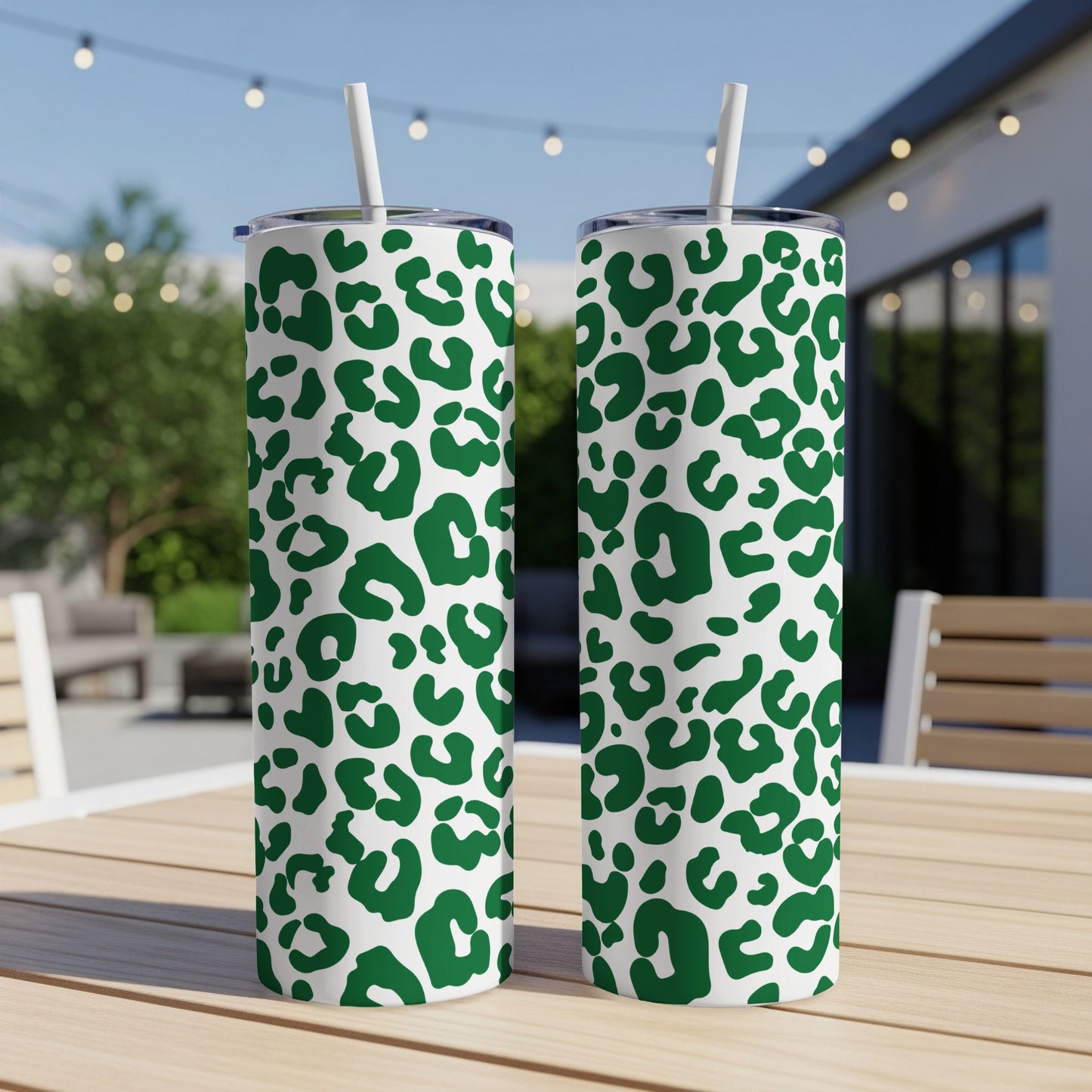 Two green leopard print tumblers with straws on a table outdoors.