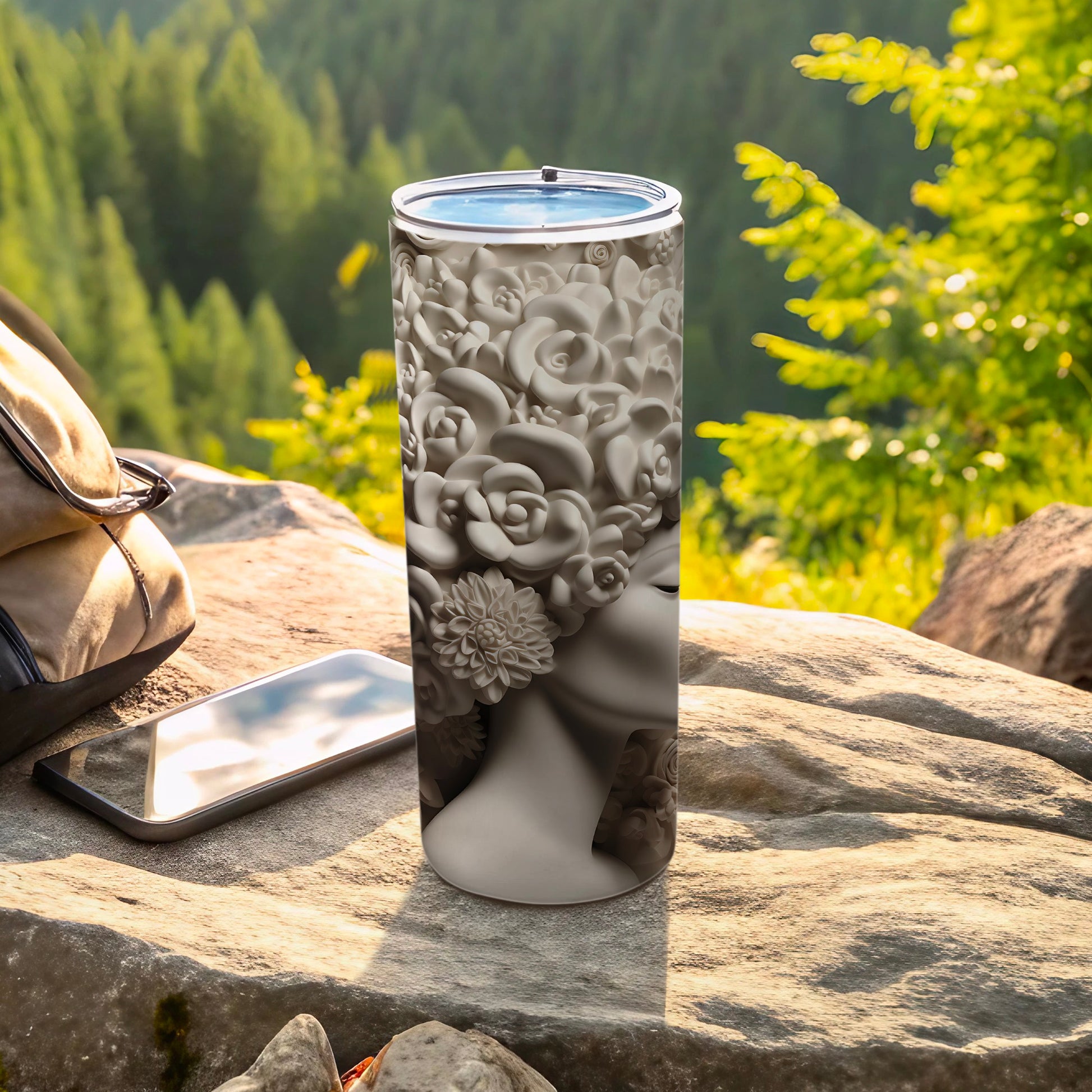 Tumbler with floral design of woman's face and hair on outdoor table.