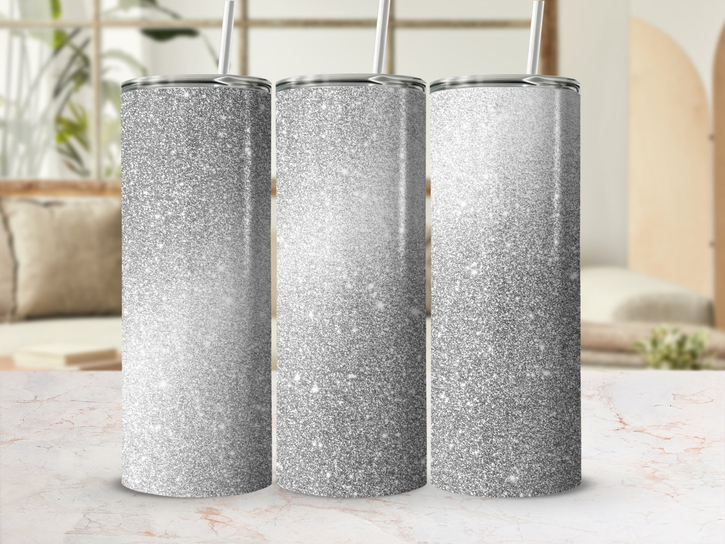 Three silver glitter tumblers with straws on a marble surface.