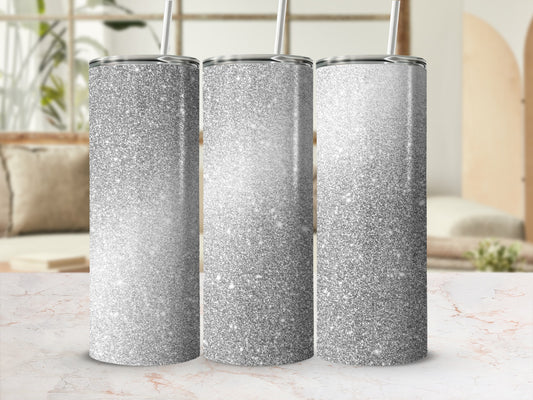 Three silver glitter tumblers with straws on a marble surface.
