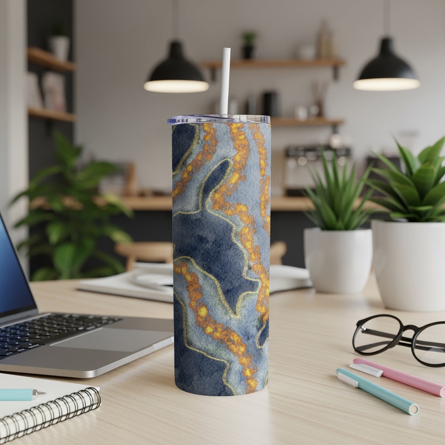Blue and gold marbled tumbler with straw on desk.